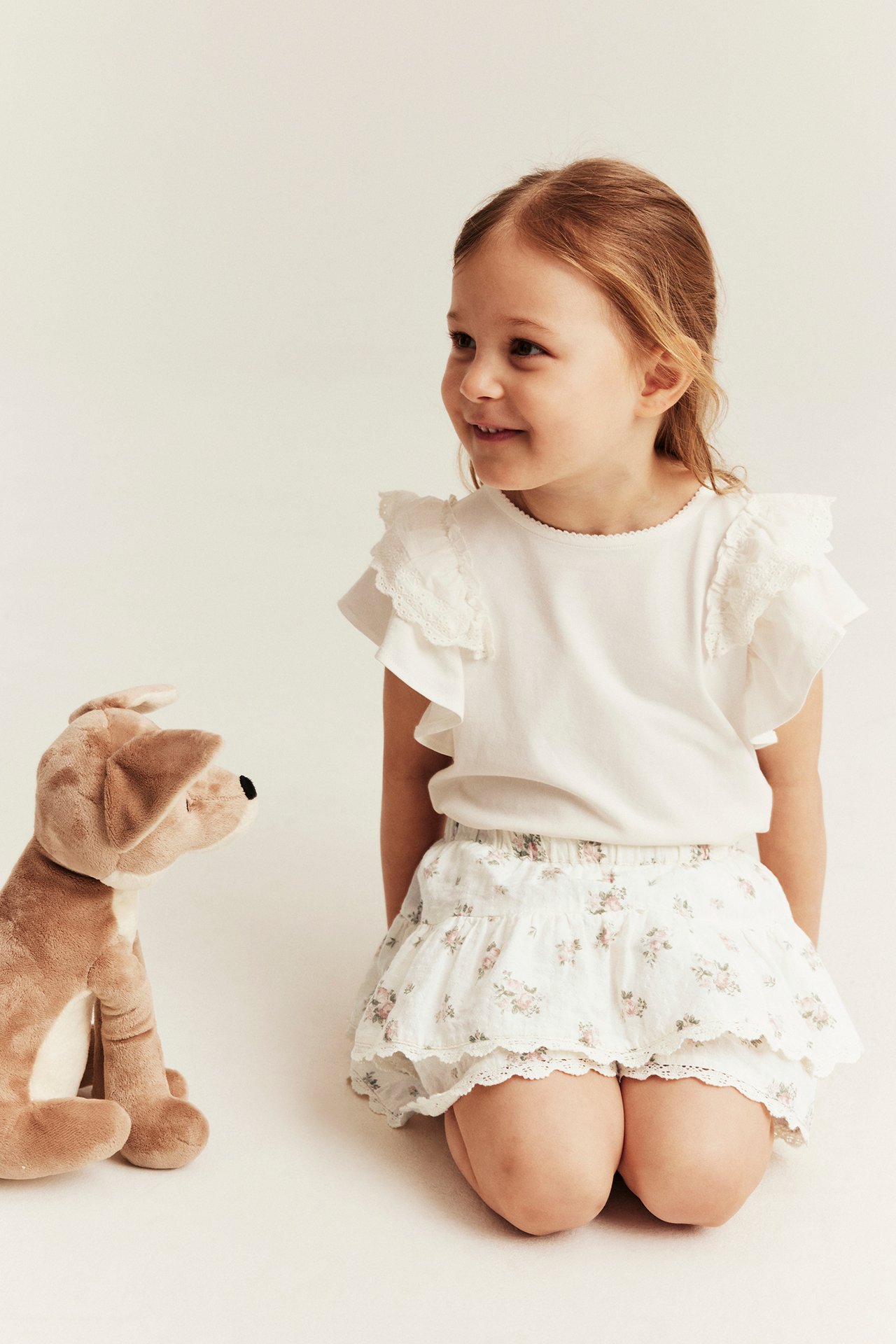 Front view: Kid wears an off-white floral ruffled cotton skort with lace trim and a white ruffled top.