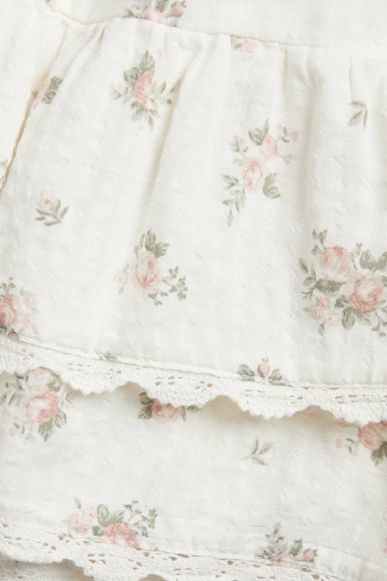 Nahaufnahme eines off-white Baumwoll-Shorts-Rocks mit rosa Blumenmuster und spitzenbesetzten Rüschen.