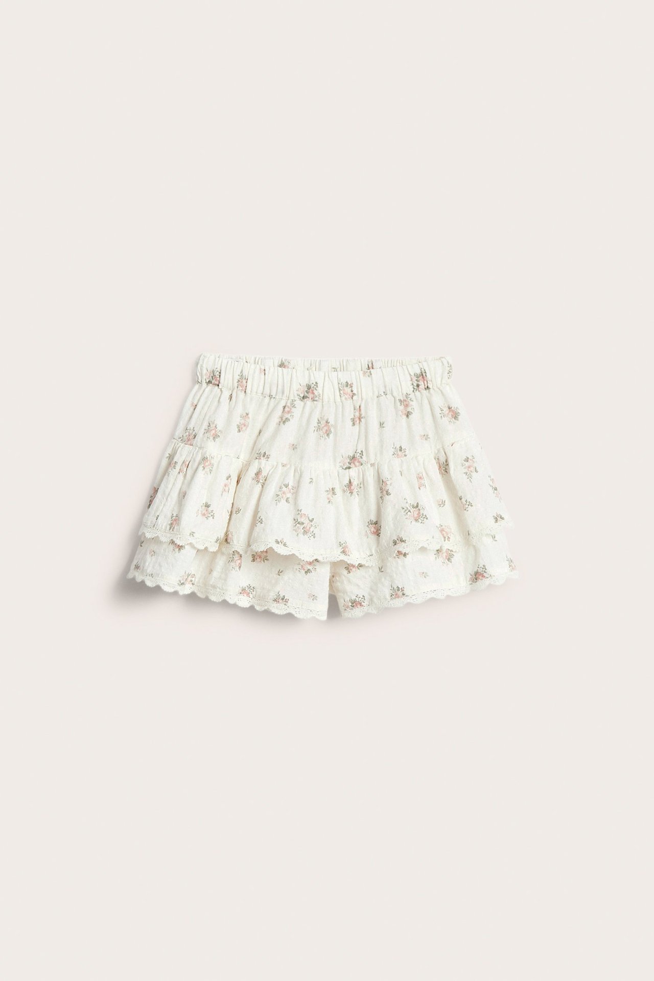 Front view of an off-white kid's cotton skort with floral print, ruffles, and lace trim.