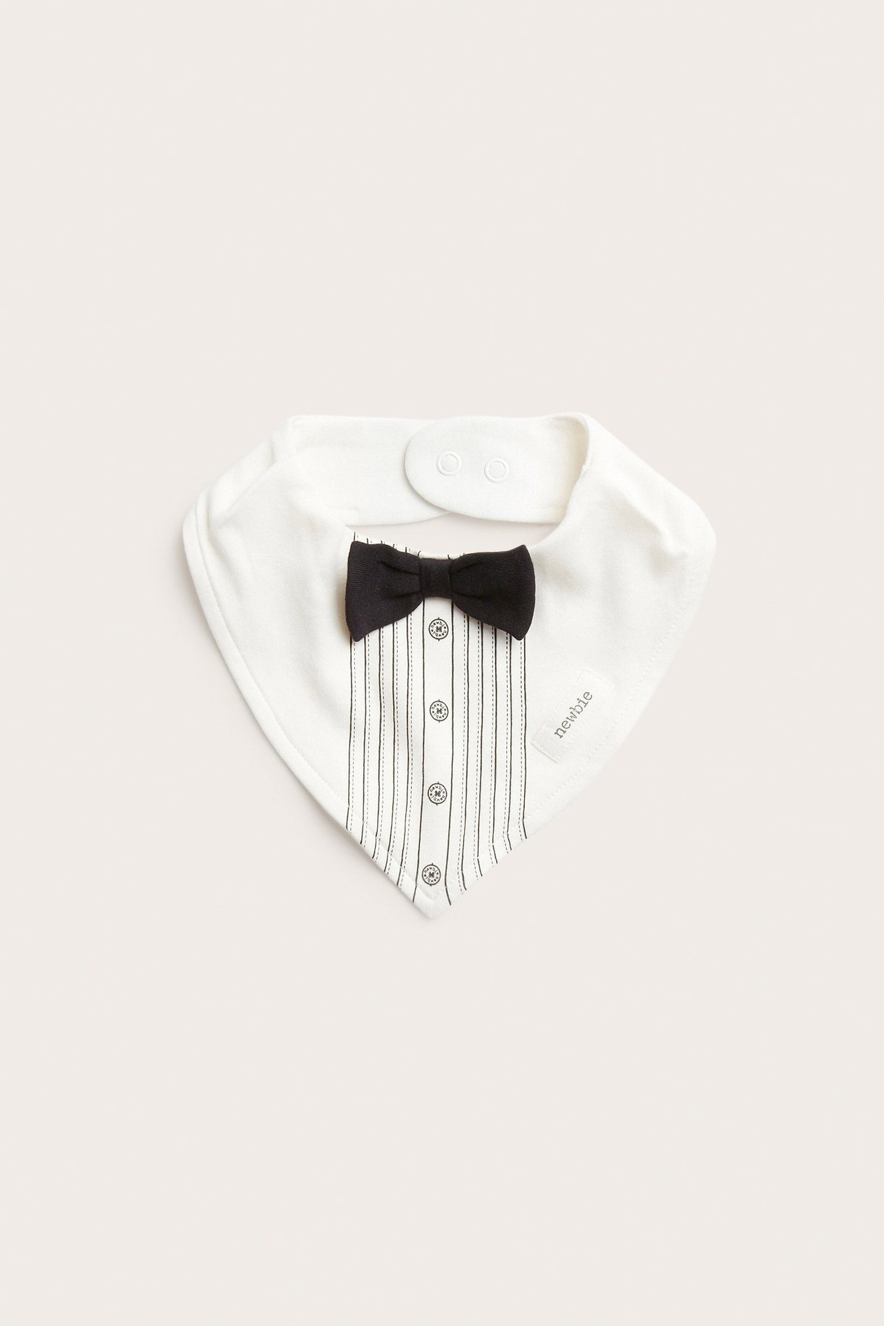 Front view: off-white baby bib with black bow tie, printed tuxedo shirt details, snap buttons.