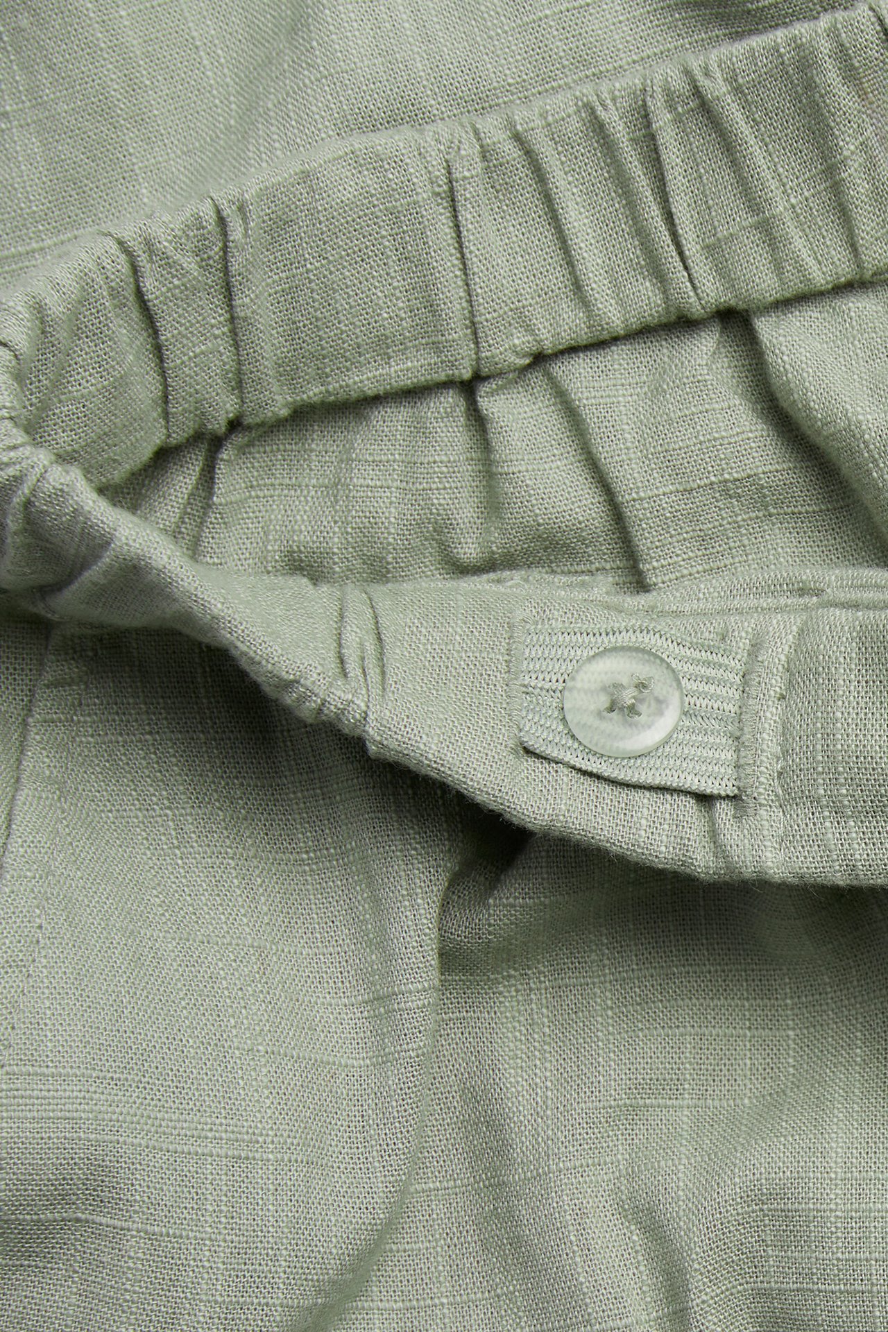 Close-up of green structured cotton trousers, showing the elasticated waistband and a clear button.