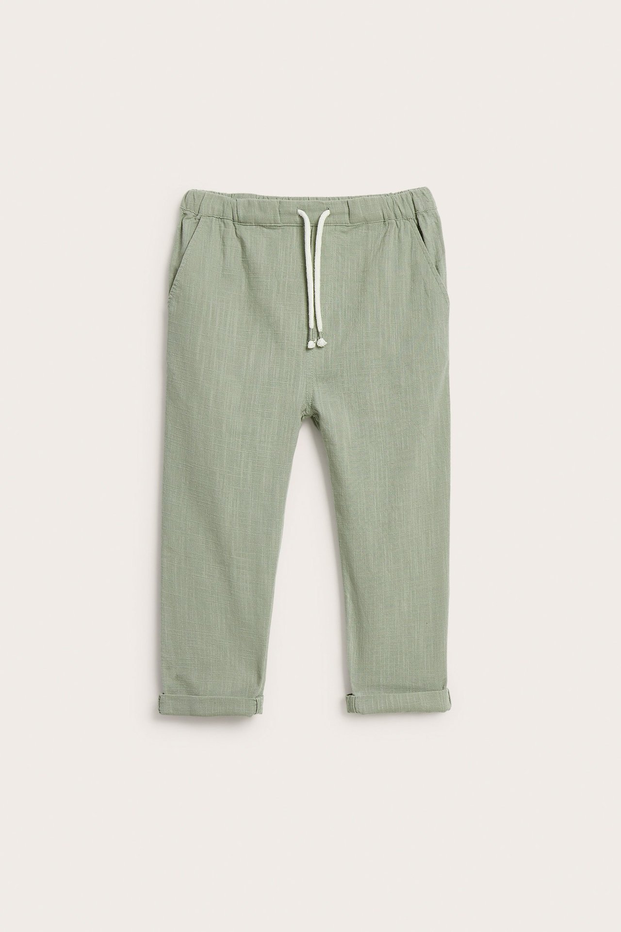 Front view of green textured cotton trousers with elastic waist, white drawstring, side pockets, and rolled-up cuffs.