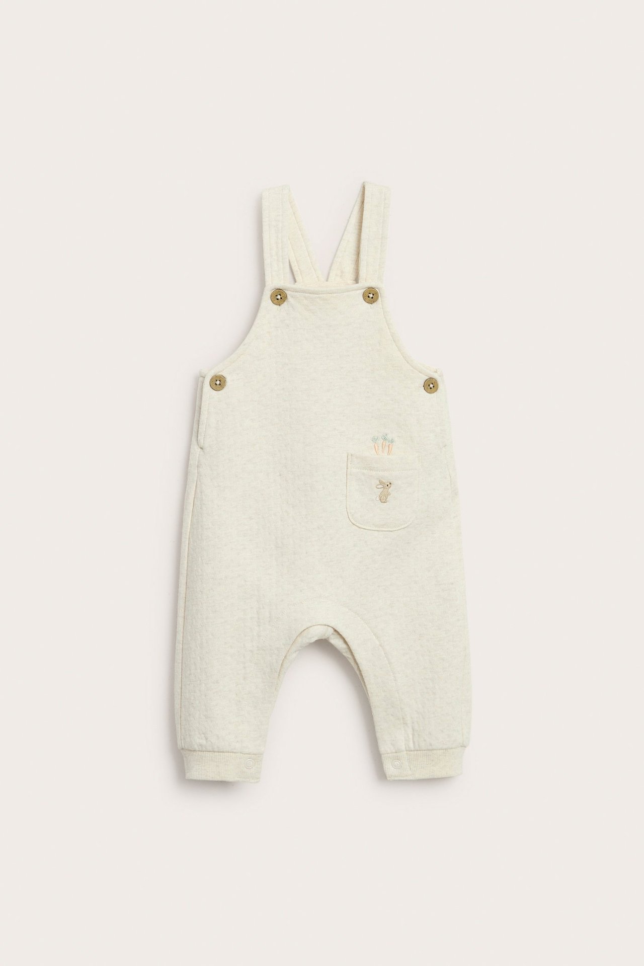 Front view of a beige melange baby jersey overall with a bunny and carrot embroidery on a front pocket.