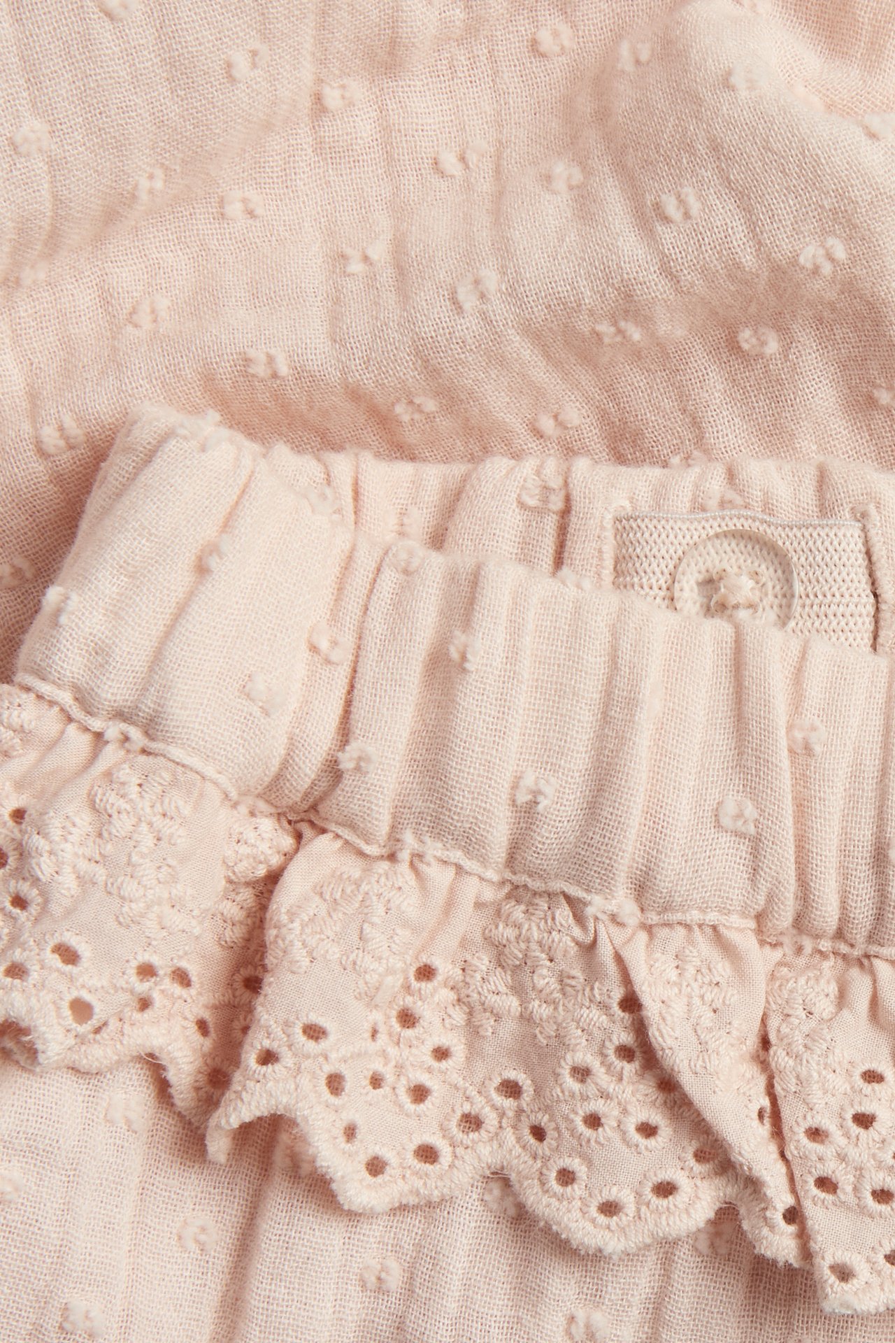 Nahaufnahme von hellrosa gewebter Baumwollhose mit Punktstruktur, elastischem Bund und Spitzenrüschen.