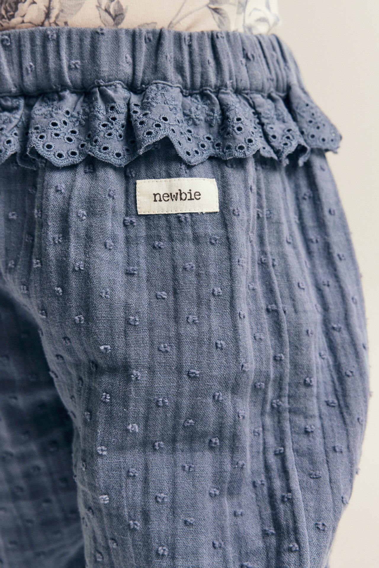 Nahaufnahme von blauen, strukturierten Baumwoll-Babyhosen mit Spitzenrüsche und Gummizug an Taille und Knöcheln.