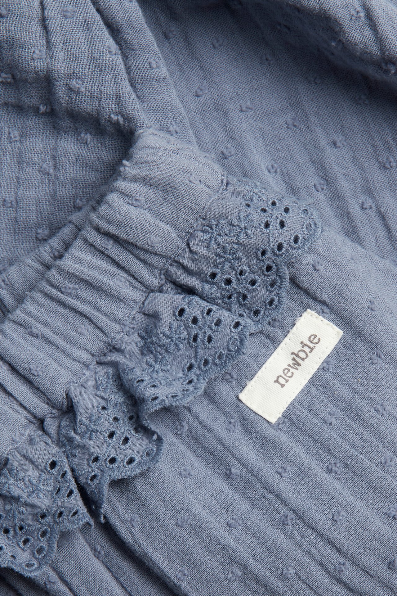 Close-up of blue textured cotton trousers with a ruffled elastic waist and eyelet lace trim.