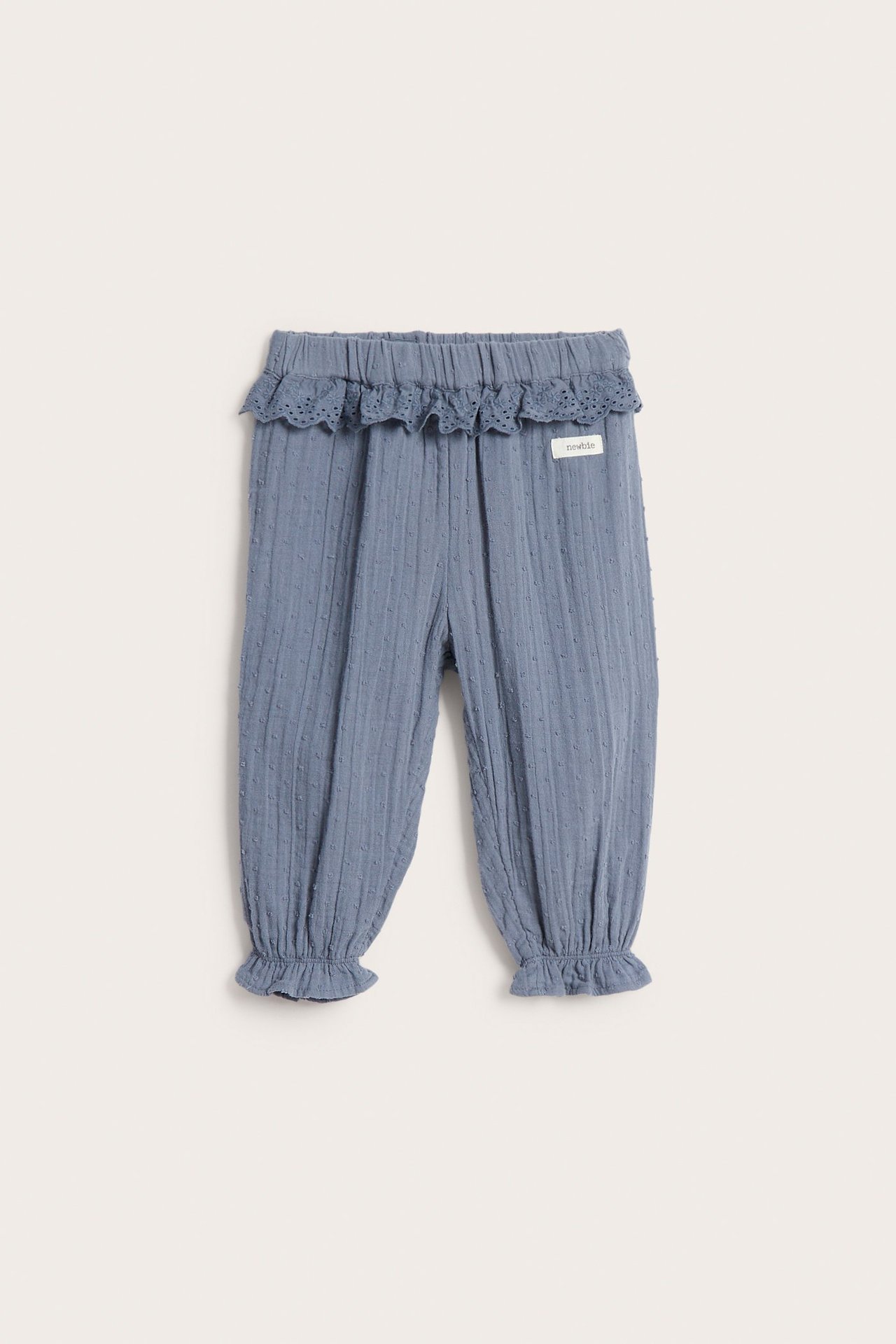 Front view: Dusty blue baby pants with subtle dot texture, lace-trimmed ruffled waist, and elasticated ruffled ankles.