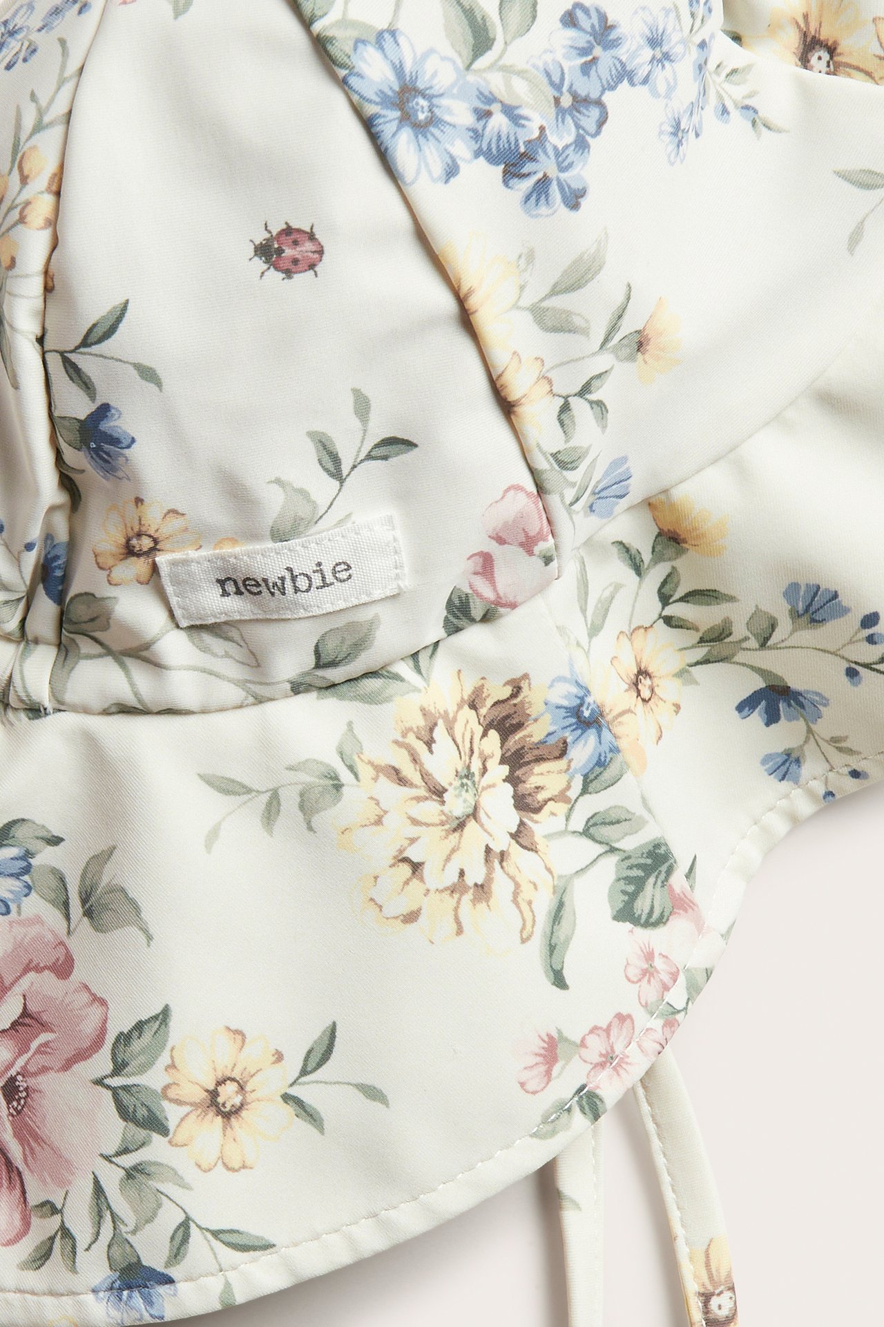 Nahaufnahme eines cremefarbenen floralen Sonnenhutes mit Bindebändern und einem Newbie-Etikett.