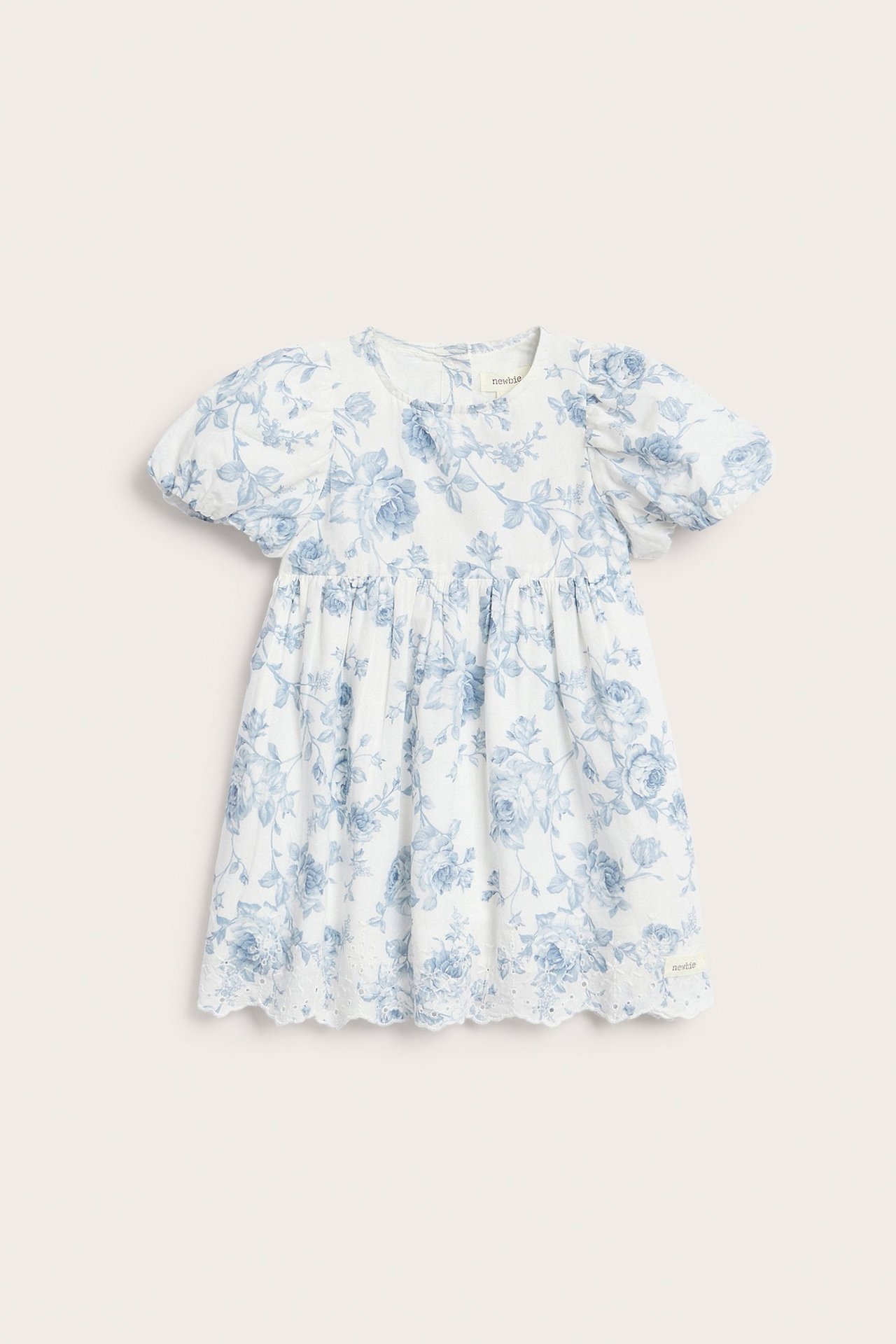 Vorderansicht eines Kinderkleides in Cremeweiß mit blauem Blumenmuster, Puffärmeln und gesticktem Saum.