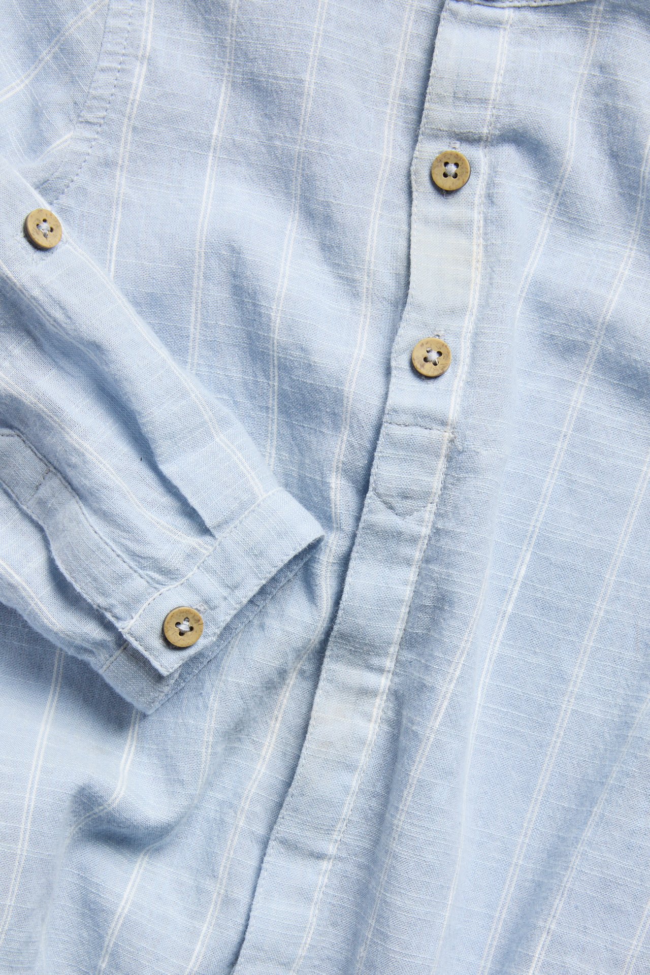 Close-up of a light blue striped long-sleeved cotton shirt-body with wooden button fastenings.