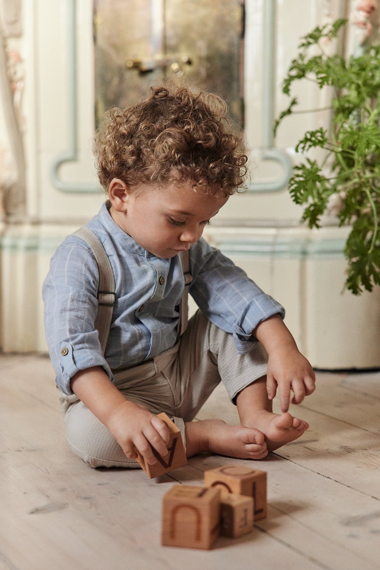 Kid in light blue striped mandarin-collar long-sleeved shirt body, beige trousers, and suspenders.