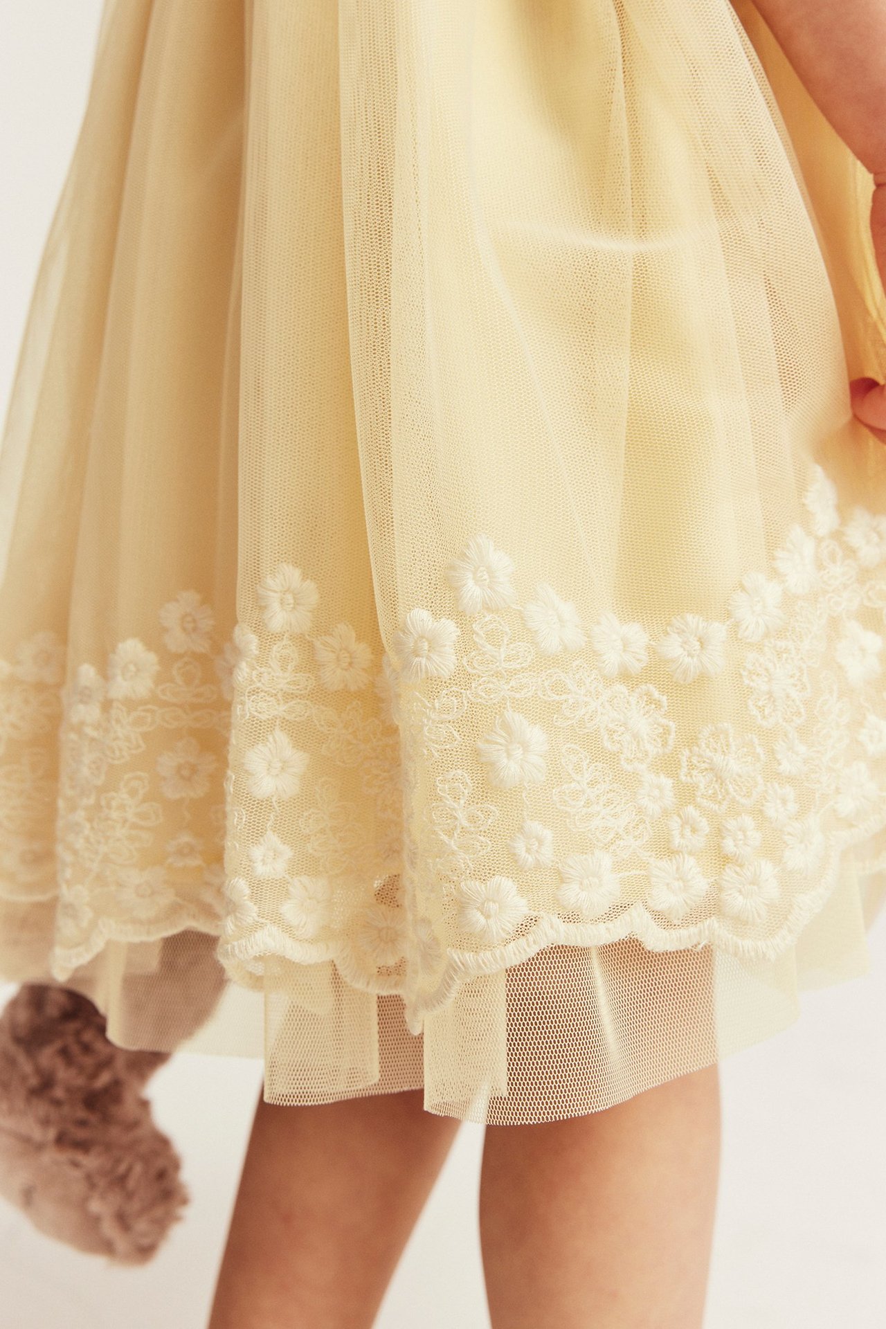 Close-up of a kid's yellow mesh dress with white floral embroidery on the hem, and layered skirt.