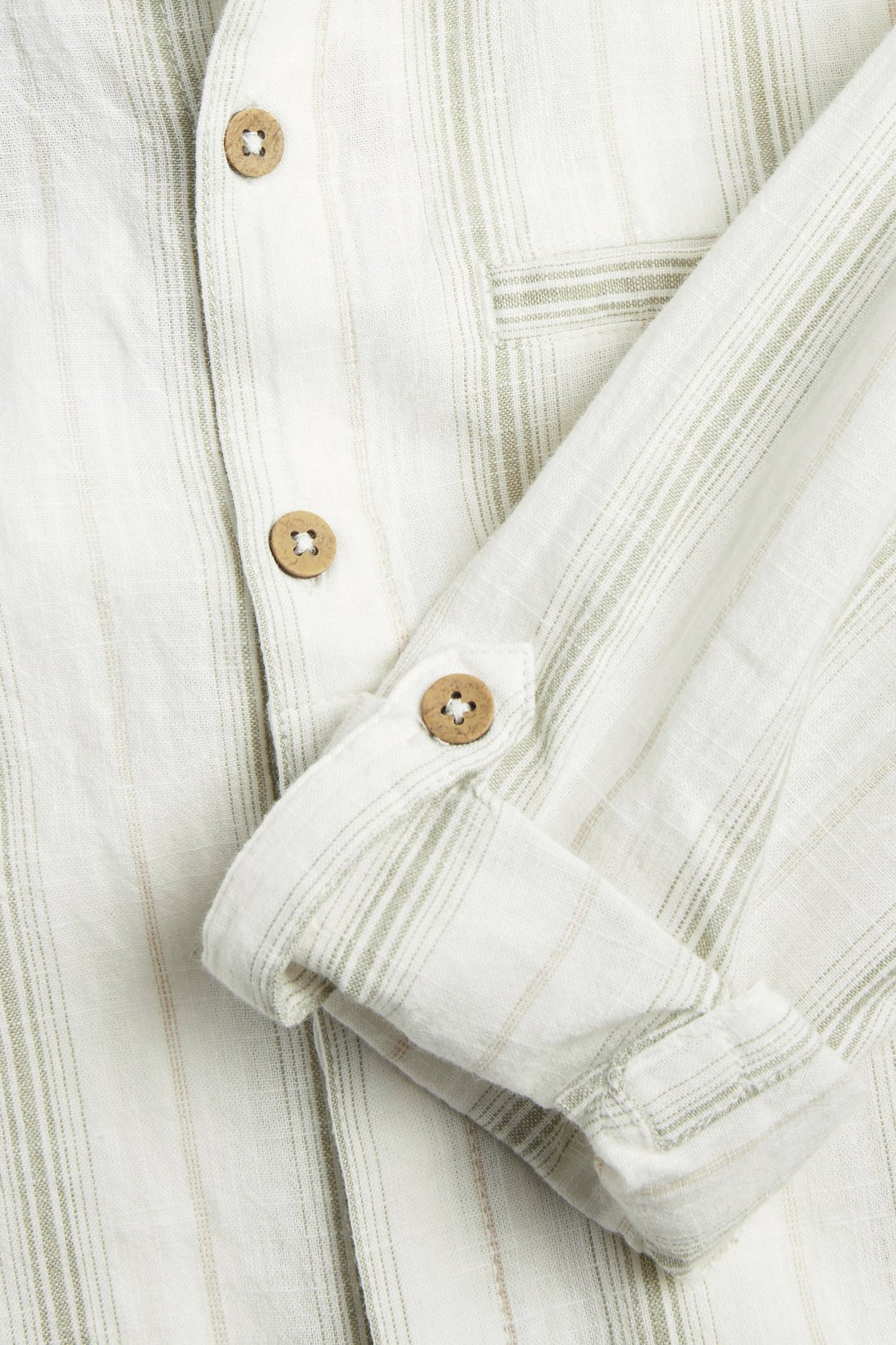 Close-up: White striped cotton grandad shirt with light green stripes, rolled-up sleeves, and wooden buttons.