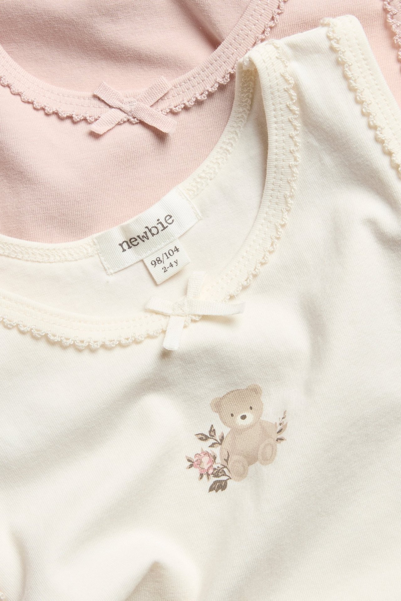 Einfärbiges offwhite Top mit Schleife, Bär und Druck, über weißem T-Shirt getragen.