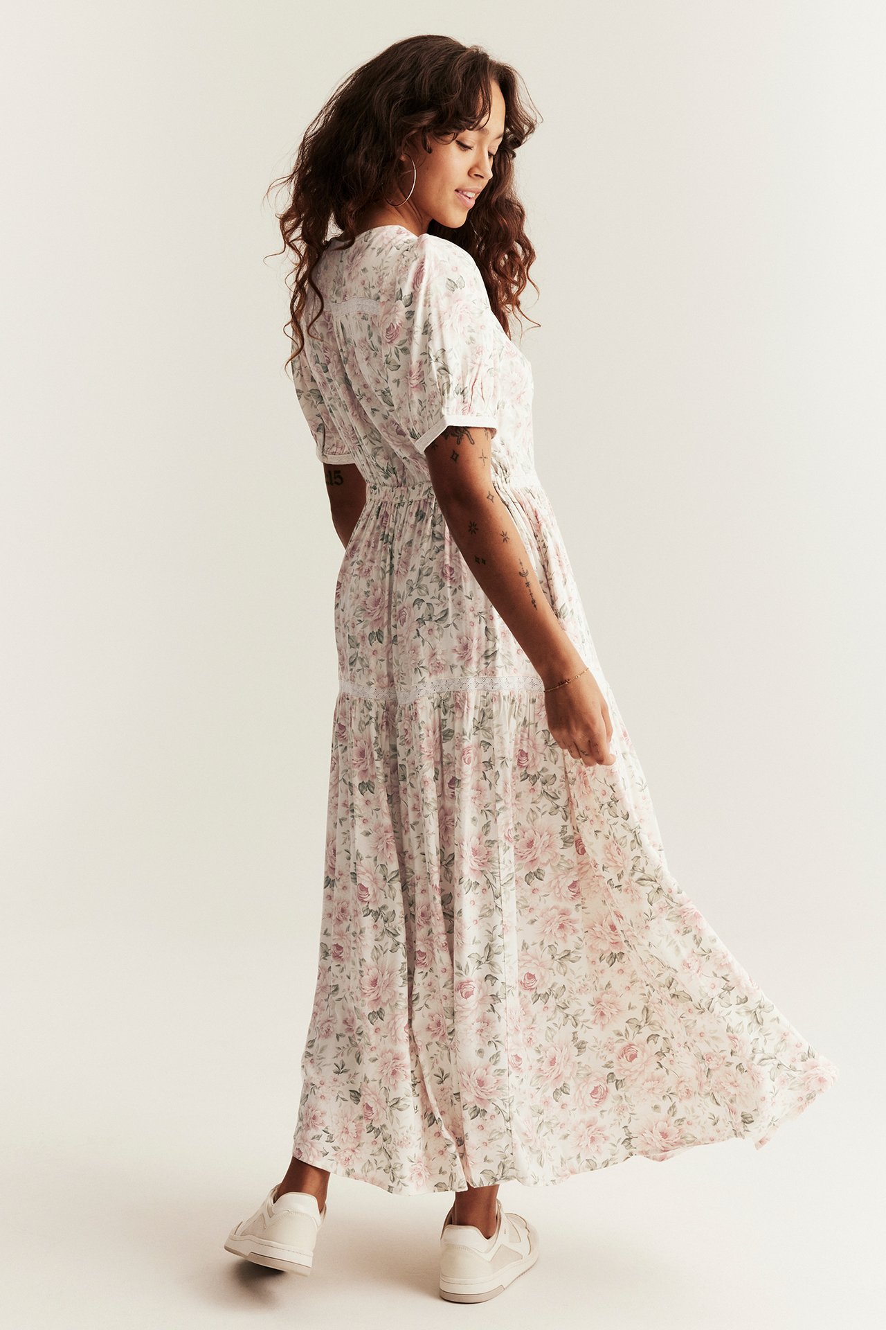 Side view of a woman wearing an offwhite floral maxi dress with puff sleeves and white sneakers.