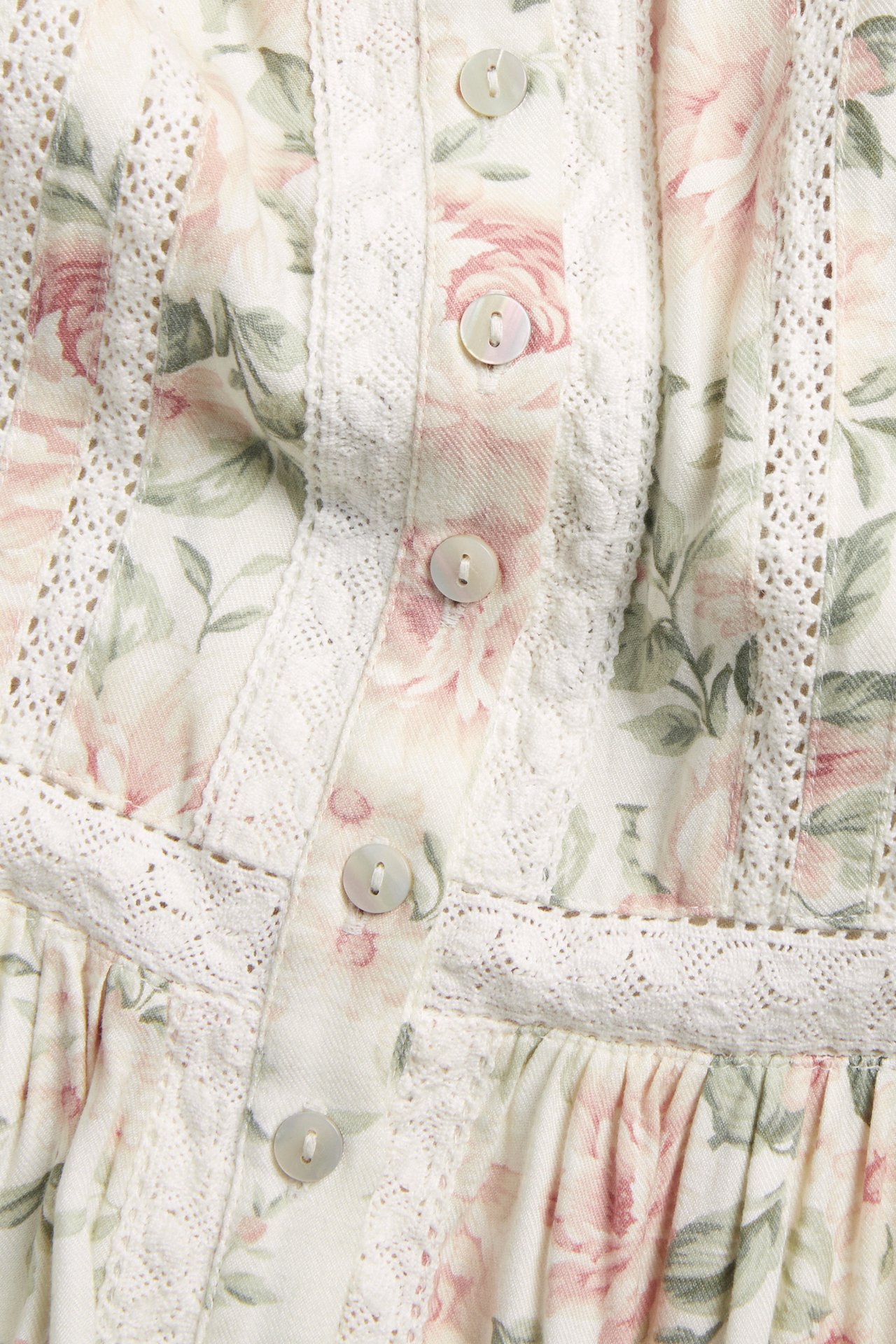 Close-up of an off-white viscose floral dress with pink roses, front buttons, and delicate lace trim.