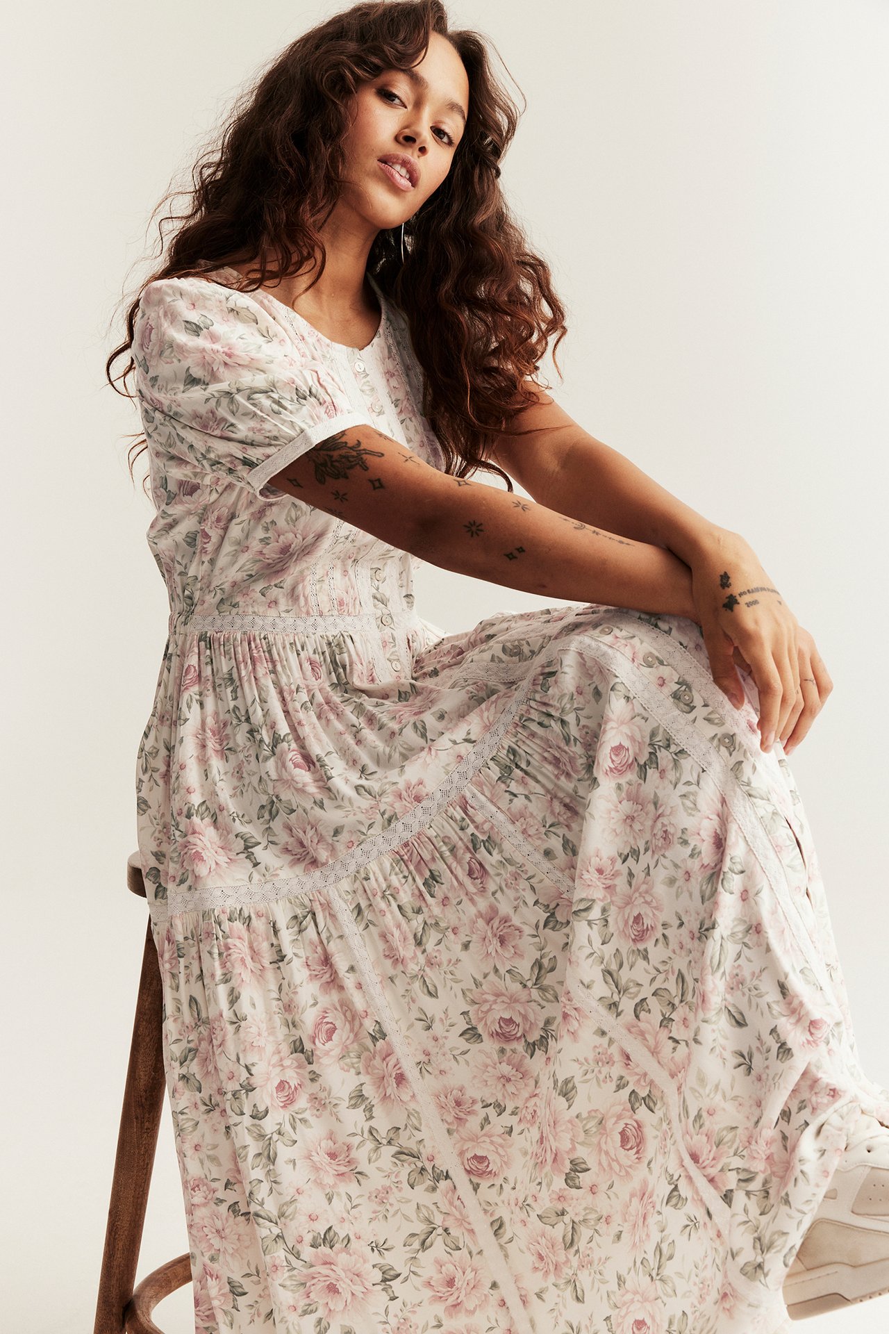 Front view of a woman sitting in an off-white floral maxi dress with puff sleeves and lace details.