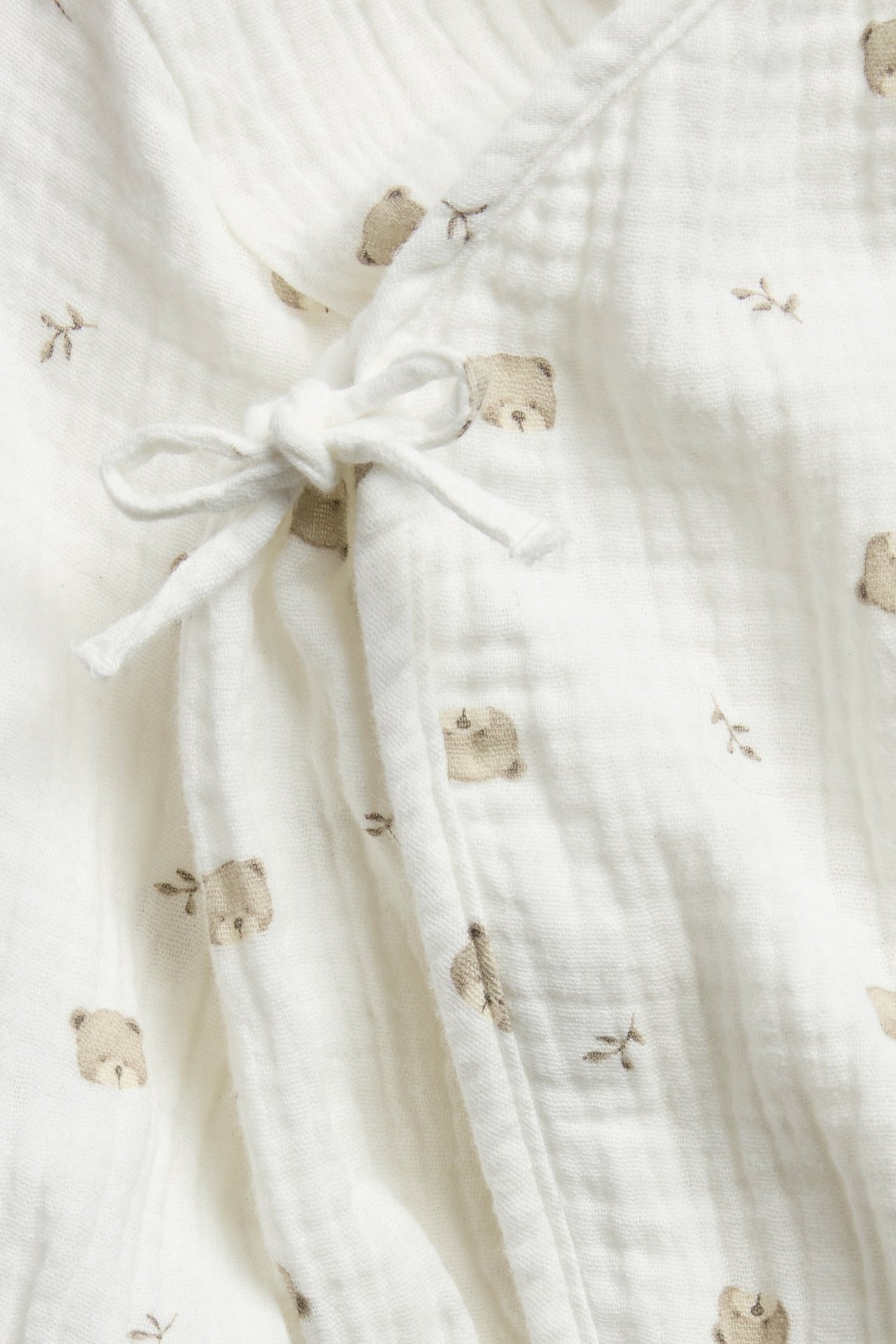 Close-up of an off-white cotton muslin baby wrap-around body with a subtle bear print and front tie closure.