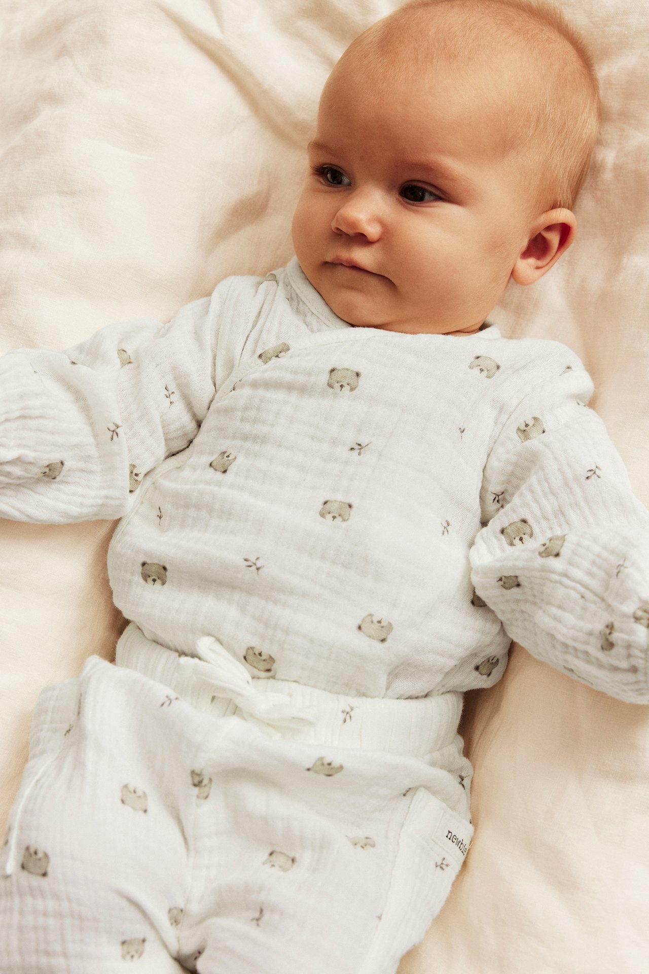 Overhead view of a baby in a white bear print muslin wrap top and matching pants.