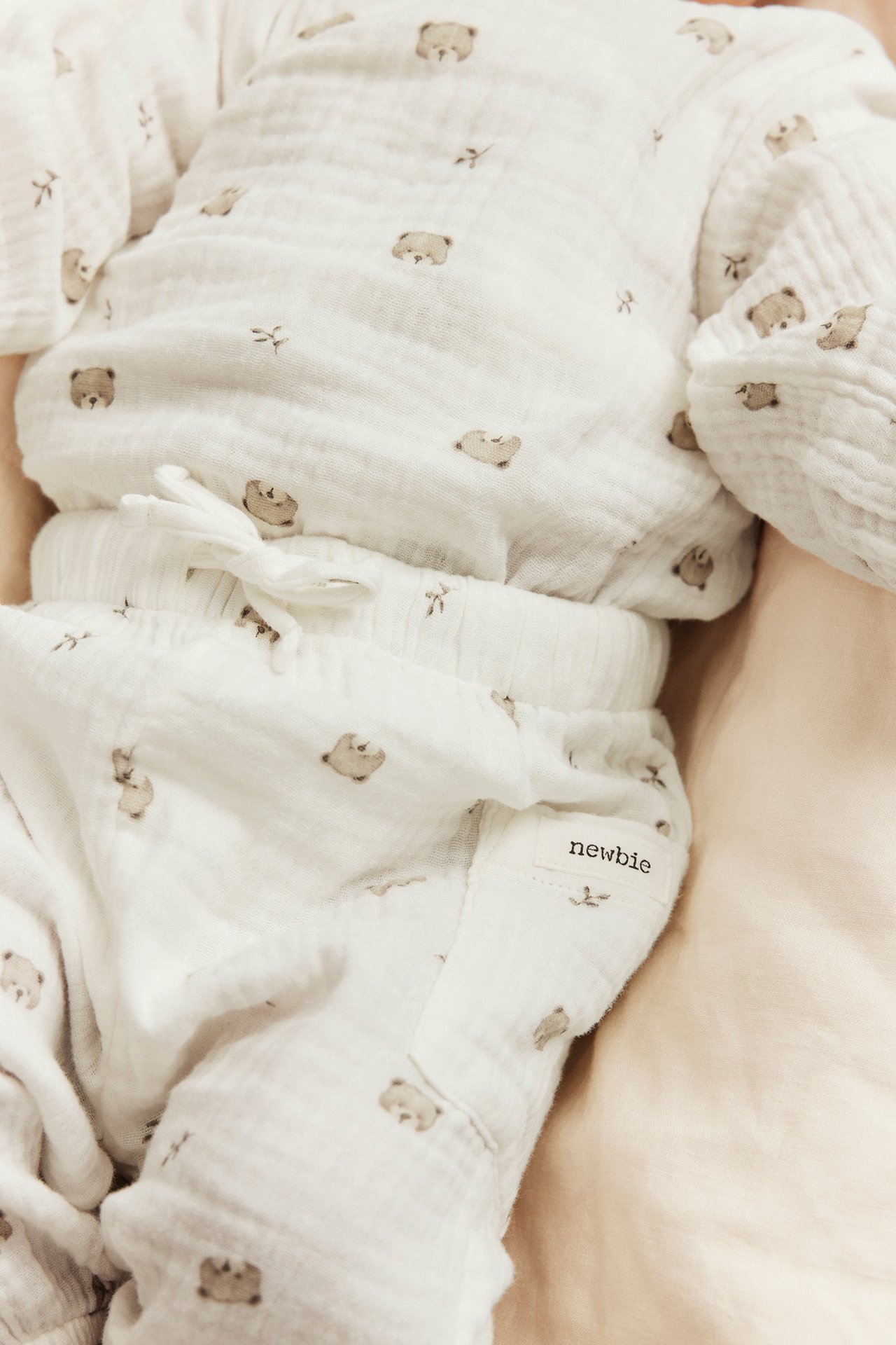 Nahaufnahme eines Babys im weißen Musselin-Pyjama-Set mit braunem Bärendruck.