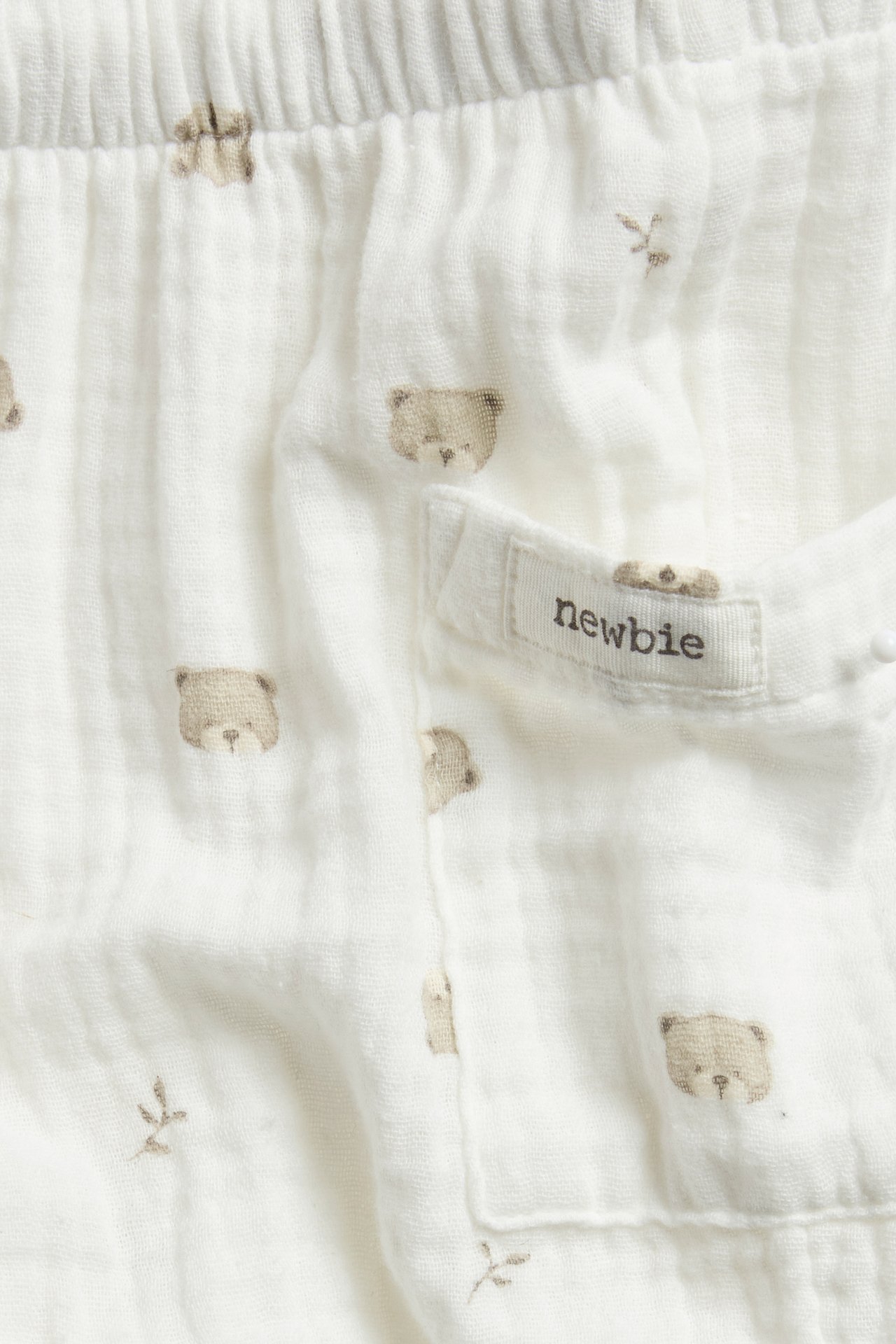 Close-up of off-white cotton muslin trousers with bear print, elastic waist, and Newbie label on pocket.