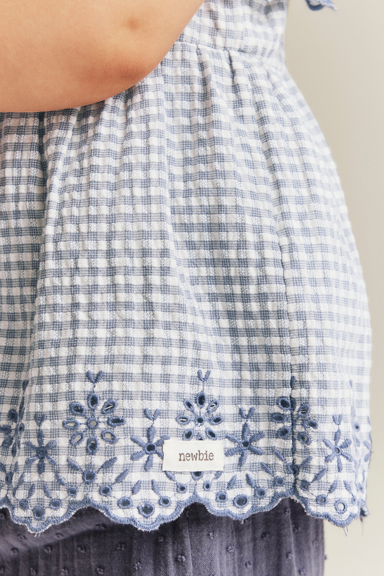 Nahaufnahme: Babys blau-weiß karierter Baumwoll-Peplum-Blusenbody mit besticktem Wellensaum.