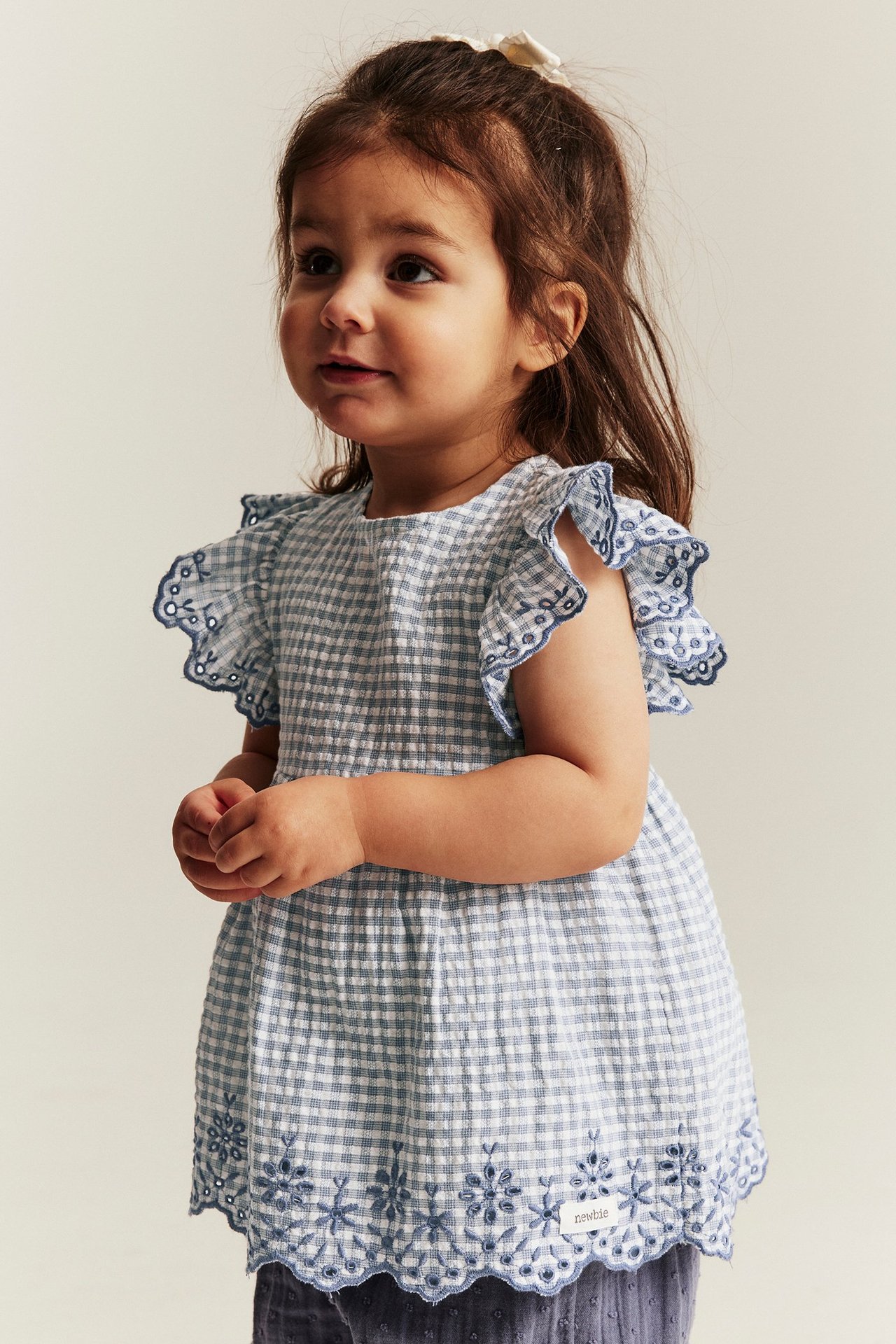 Front view baby girl in blue checked cotton body with embroidered ruffled sleeves and hem.