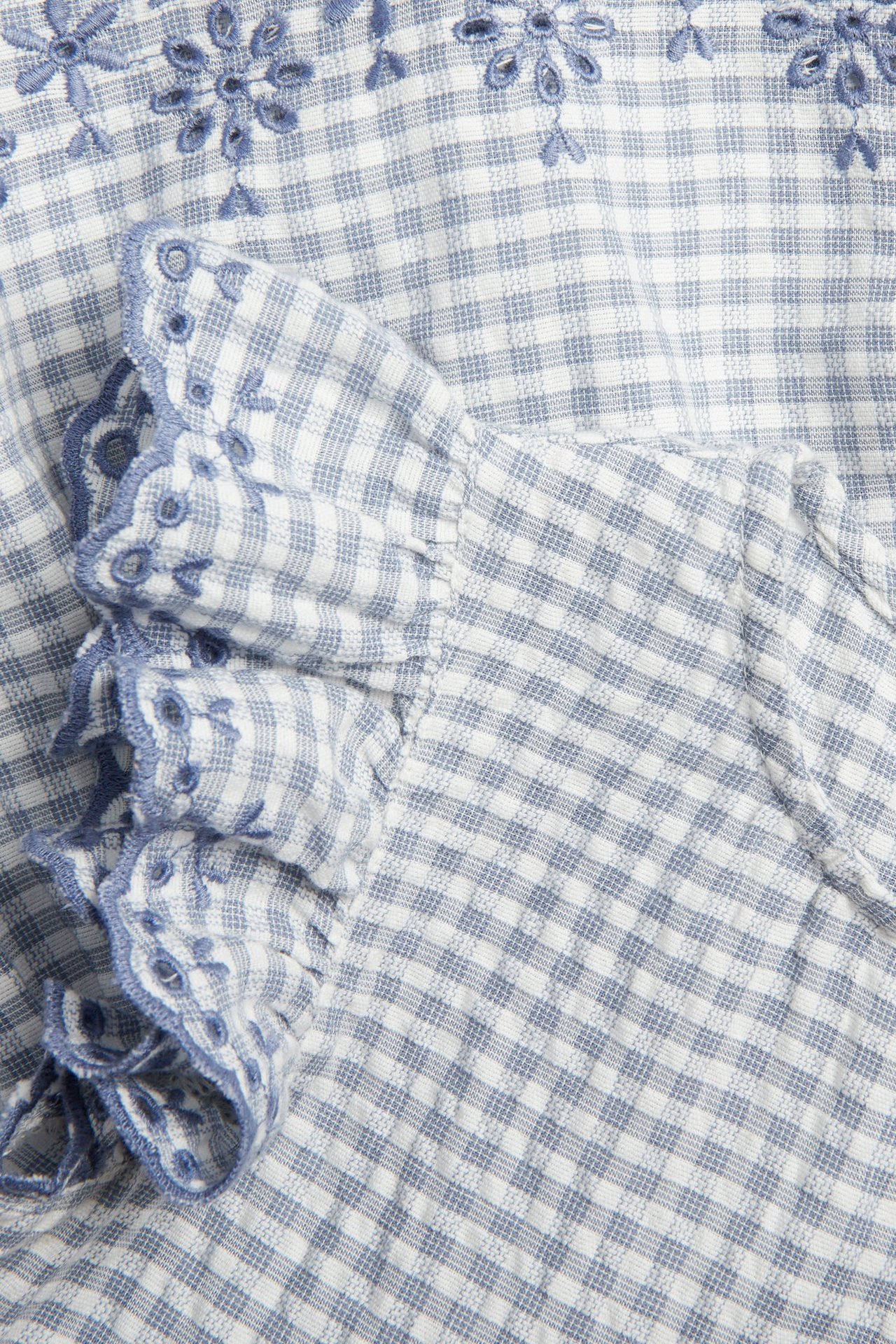 Close-up of a blue and white checked cotton peplum blouse with blue embroidered floral edges.