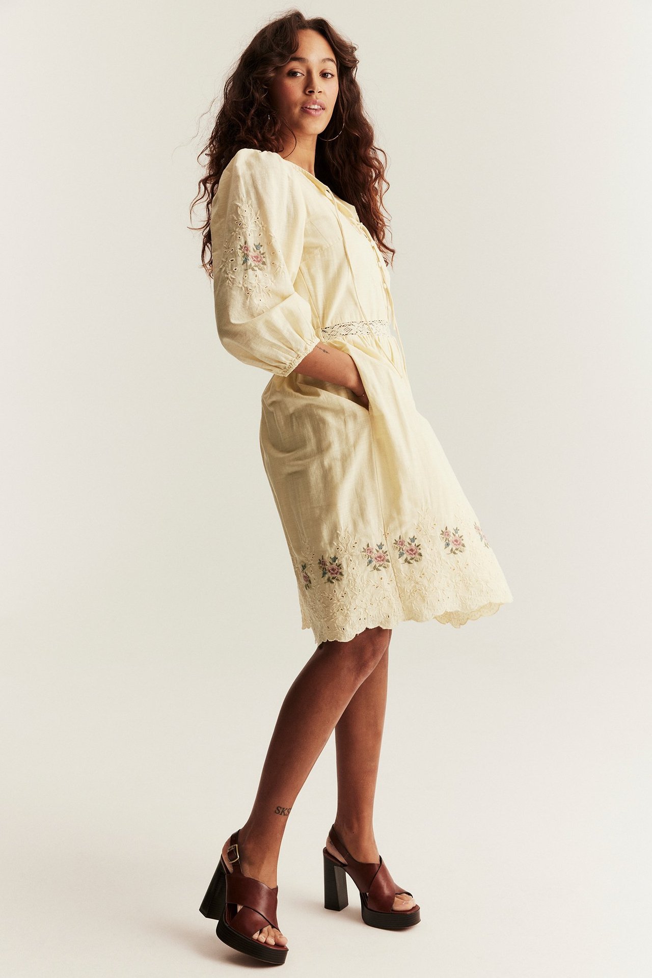 Front view of a woman wearing a light yellow embroidered short dress and dark brown platform sandals.