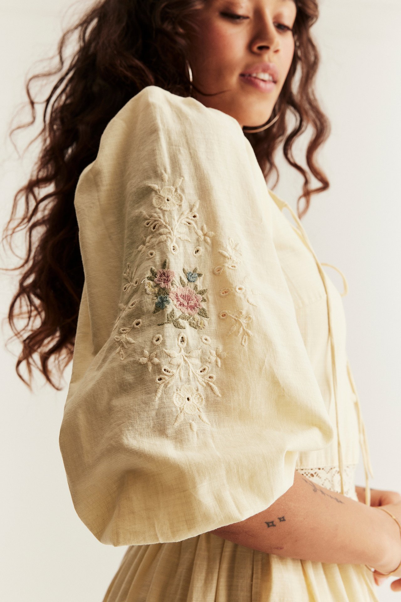 Woman in a pale yellow embroidered dress with broderie anglaise puff sleeves. Close-up.
