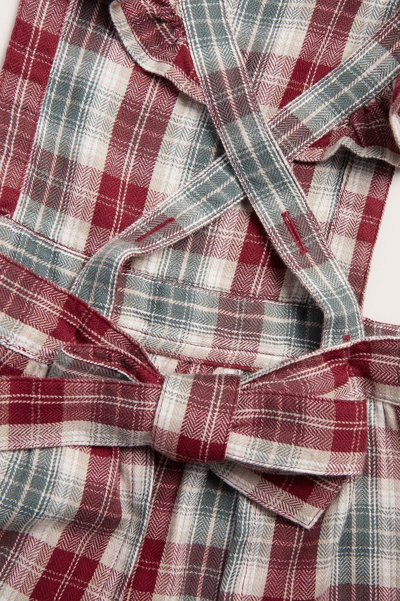 Close-up of a kid's red, beige, grey plaid cotton apron with ruffled straps and a back tie.
