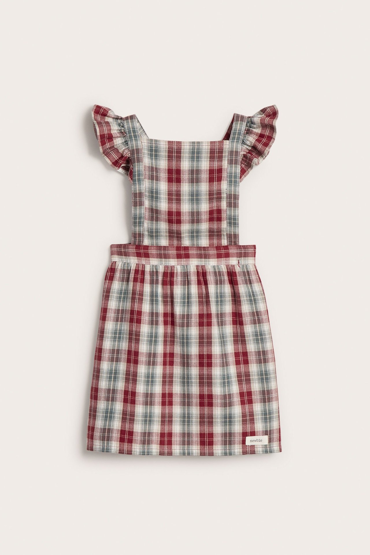 Front view of a kid's red, white, and grey plaid cotton apron dress with ruffled shoulder straps.