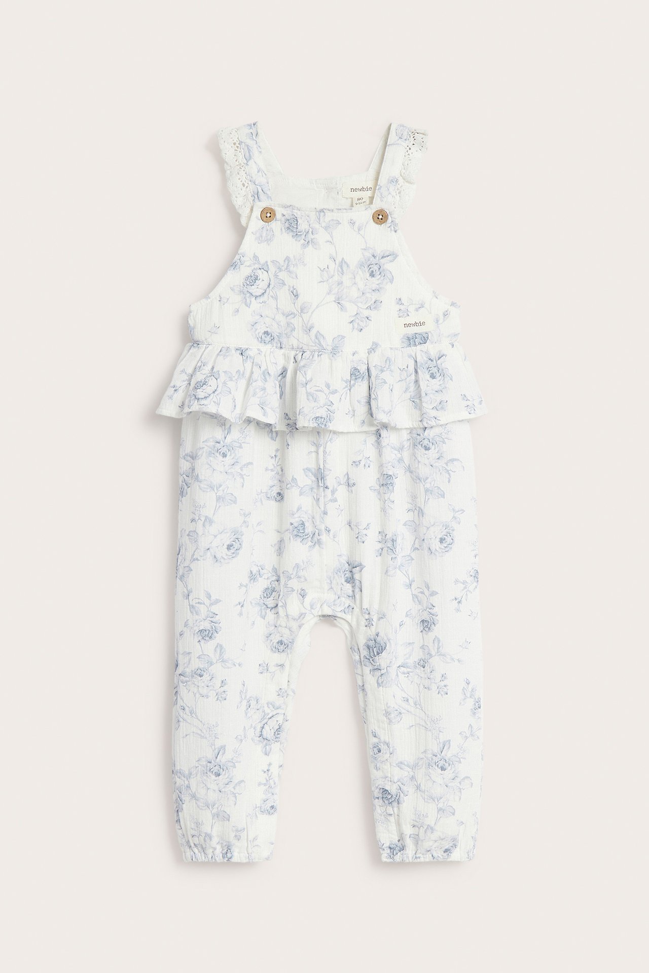 Front view: Off-white baby floral overall with waist ruffle, lace trim, and button straps.