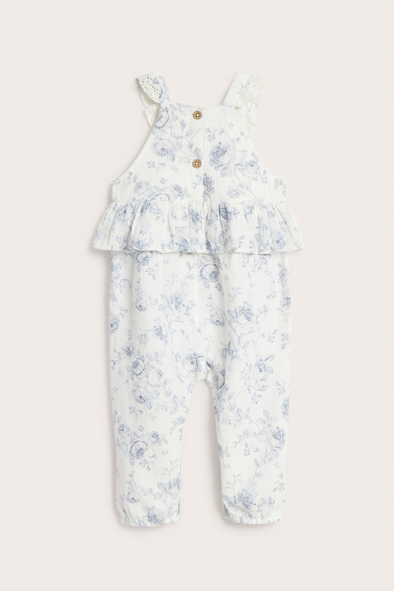 Front view of off-white baby floral cotton dungarees with waist ruffle, lace straps, and wooden buttons.