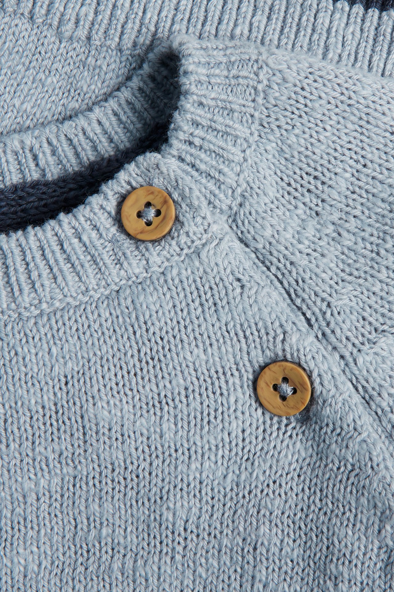 Close-up of a light blue cotton knitted sweater with ribbed neckline and two round wooden buttons.