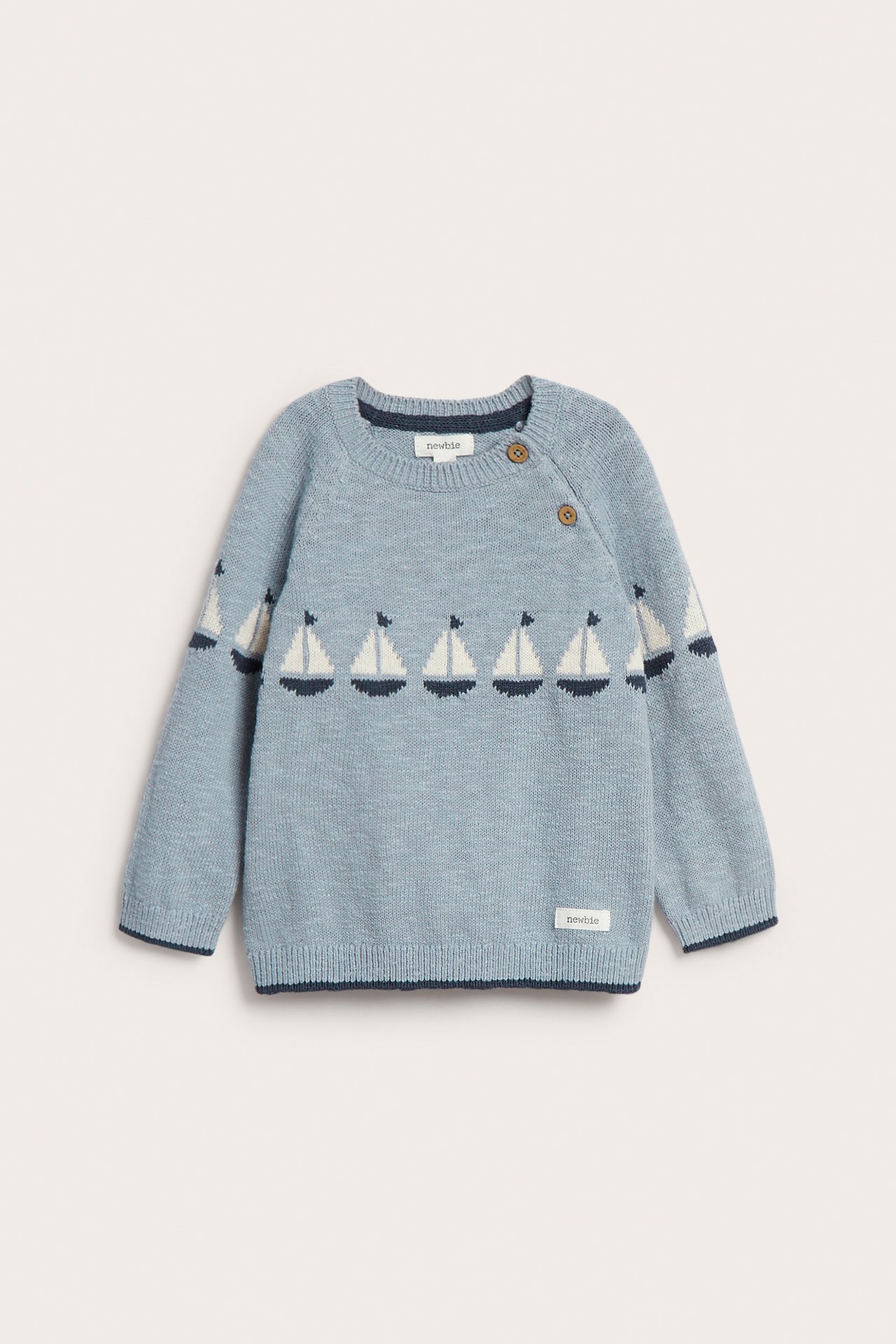 Front view of a light blue knitted cotton sweater with a white and navy jacquard sailboat pattern and shoulder buttons.