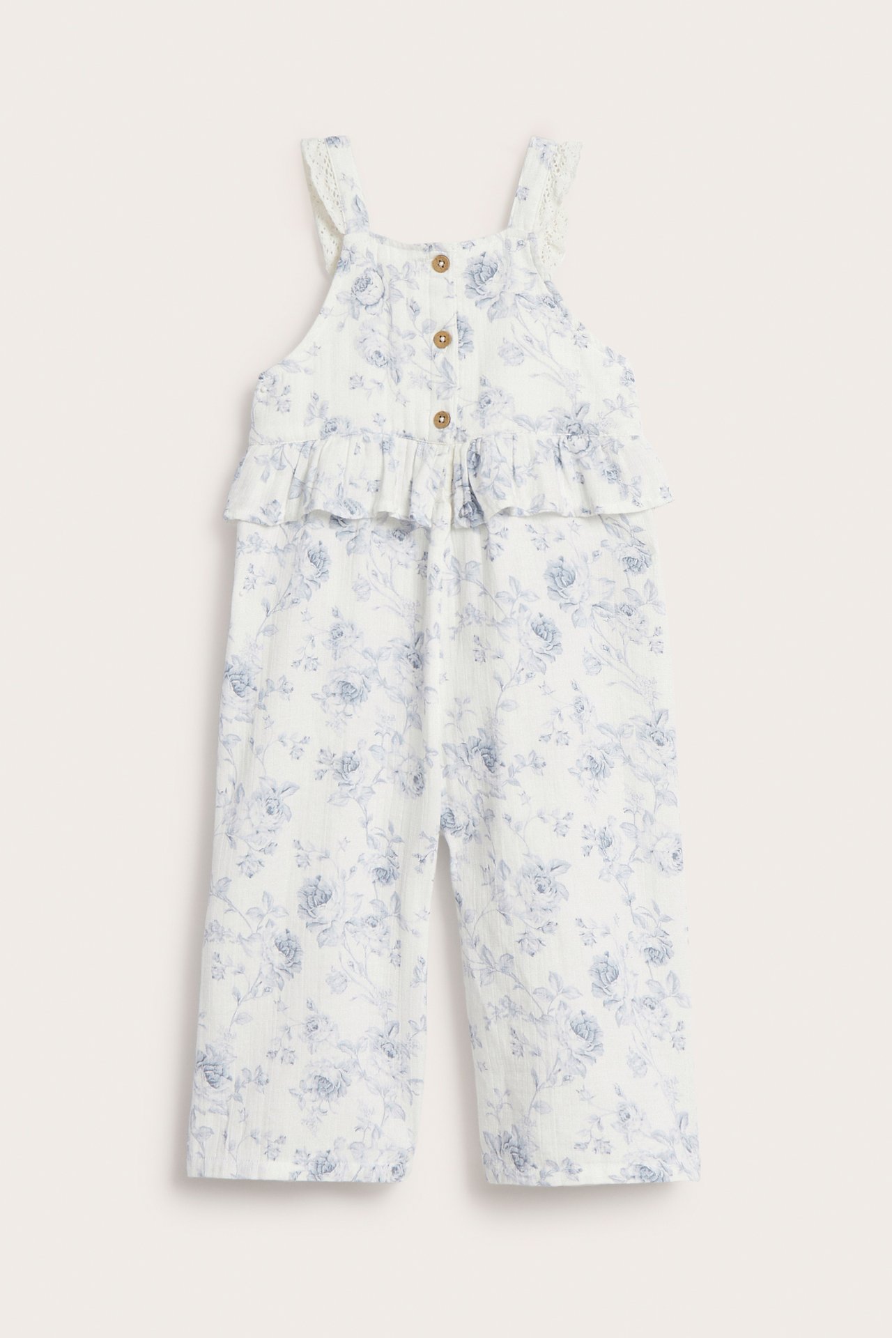 Vorderansicht eines cremefarbenen Baumwoll-Overalls mit Blumenmuster, Taillenrüsche, Spitzen-Trägern und Knöpfen vorne.