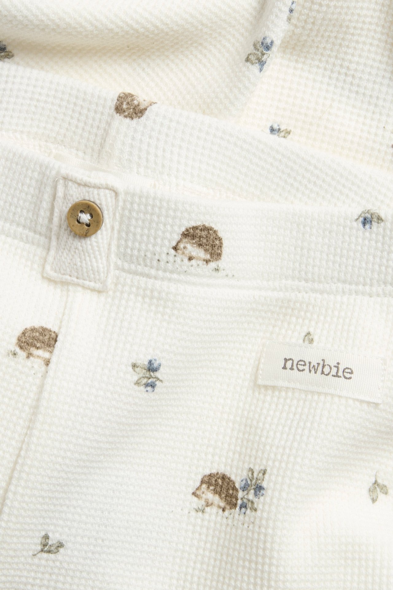 Close-up of offwhite waffle knit baby leggings with hedgehog pattern and a decorative button.
