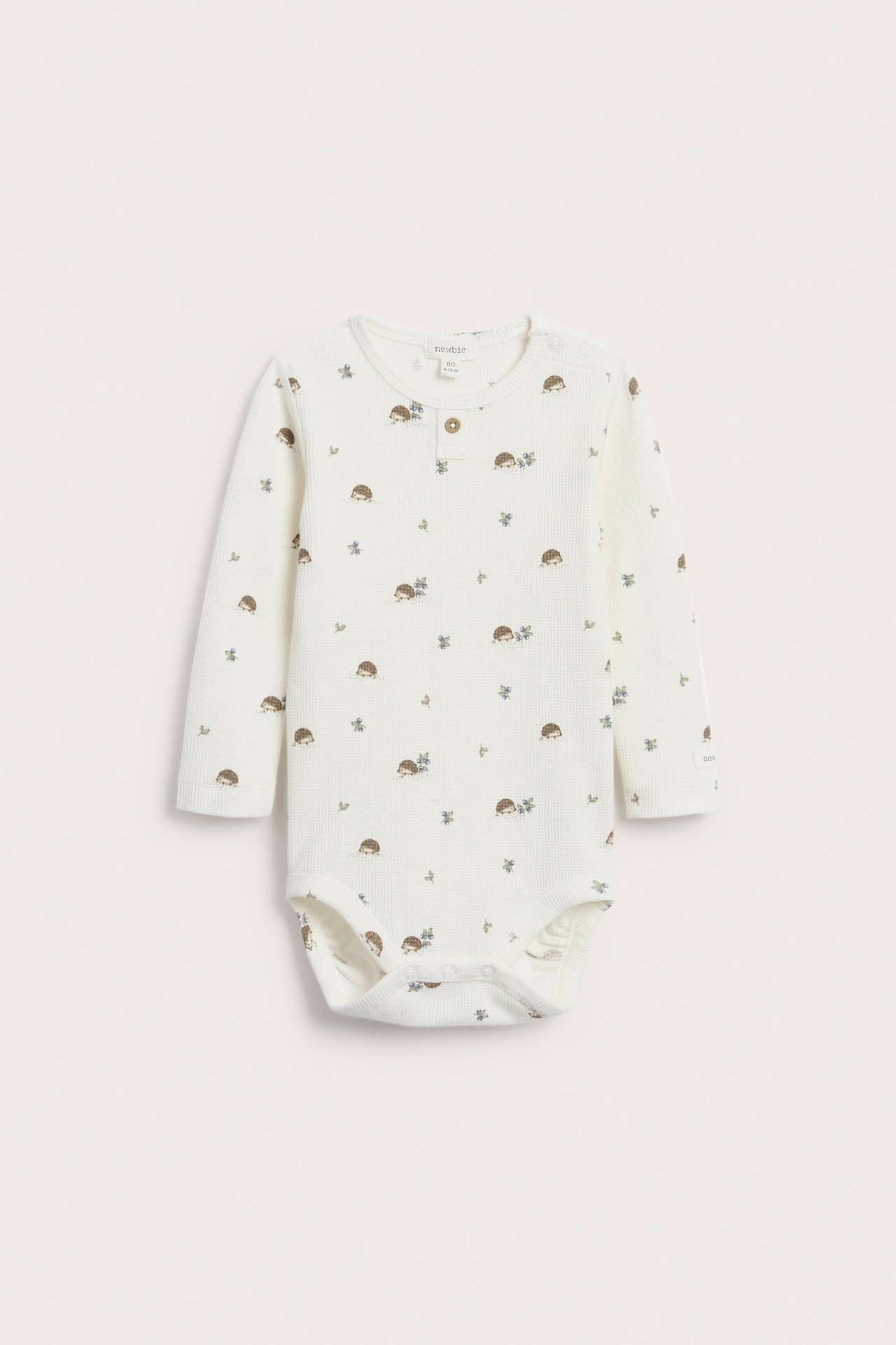 Front view of an off-white baby long-sleeved waffle bodysuit with hedgehog pattern and front buttons.