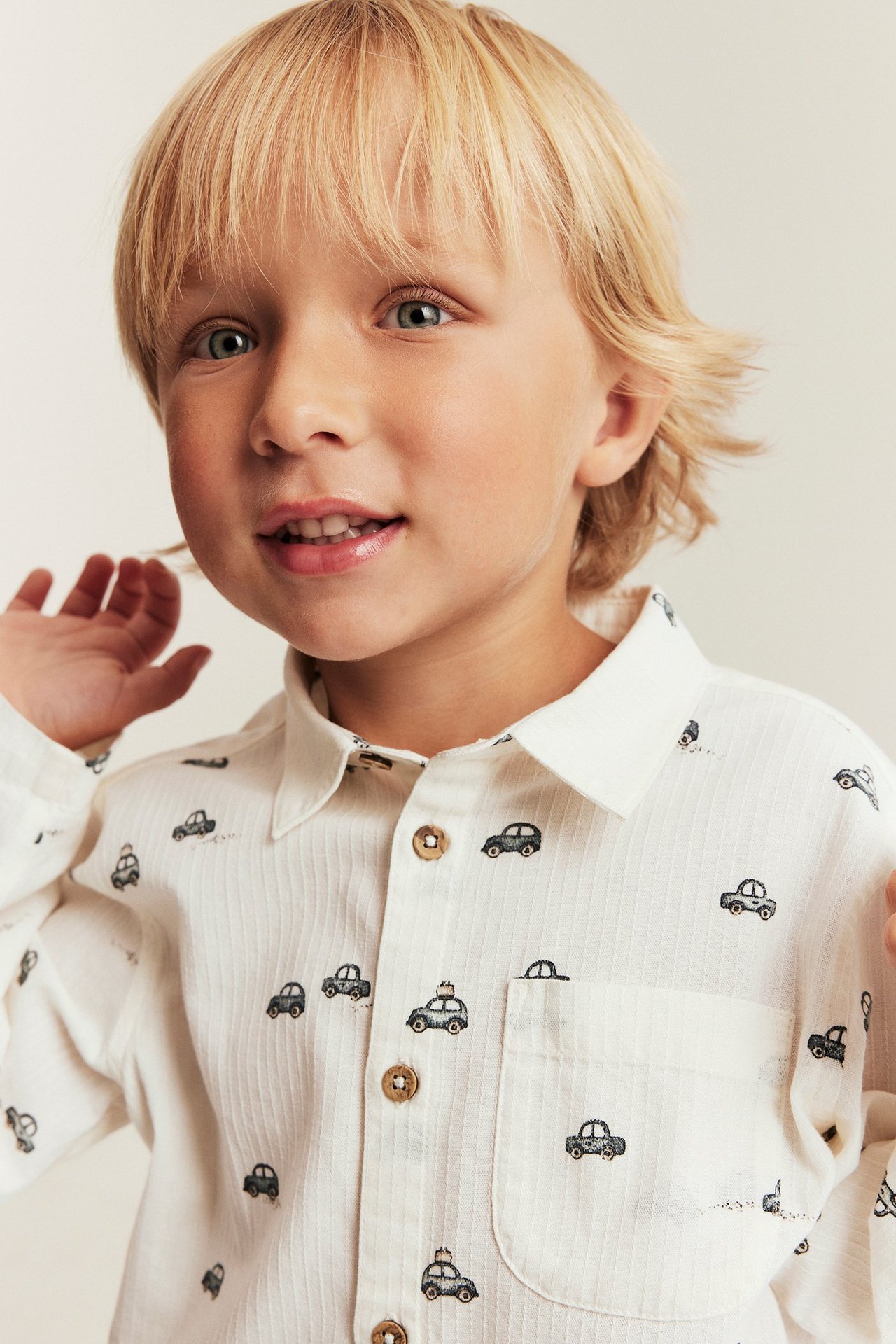 Front view of a kid wearing an off-white ribbed cotton shirt with a black car pattern and brown buttons.