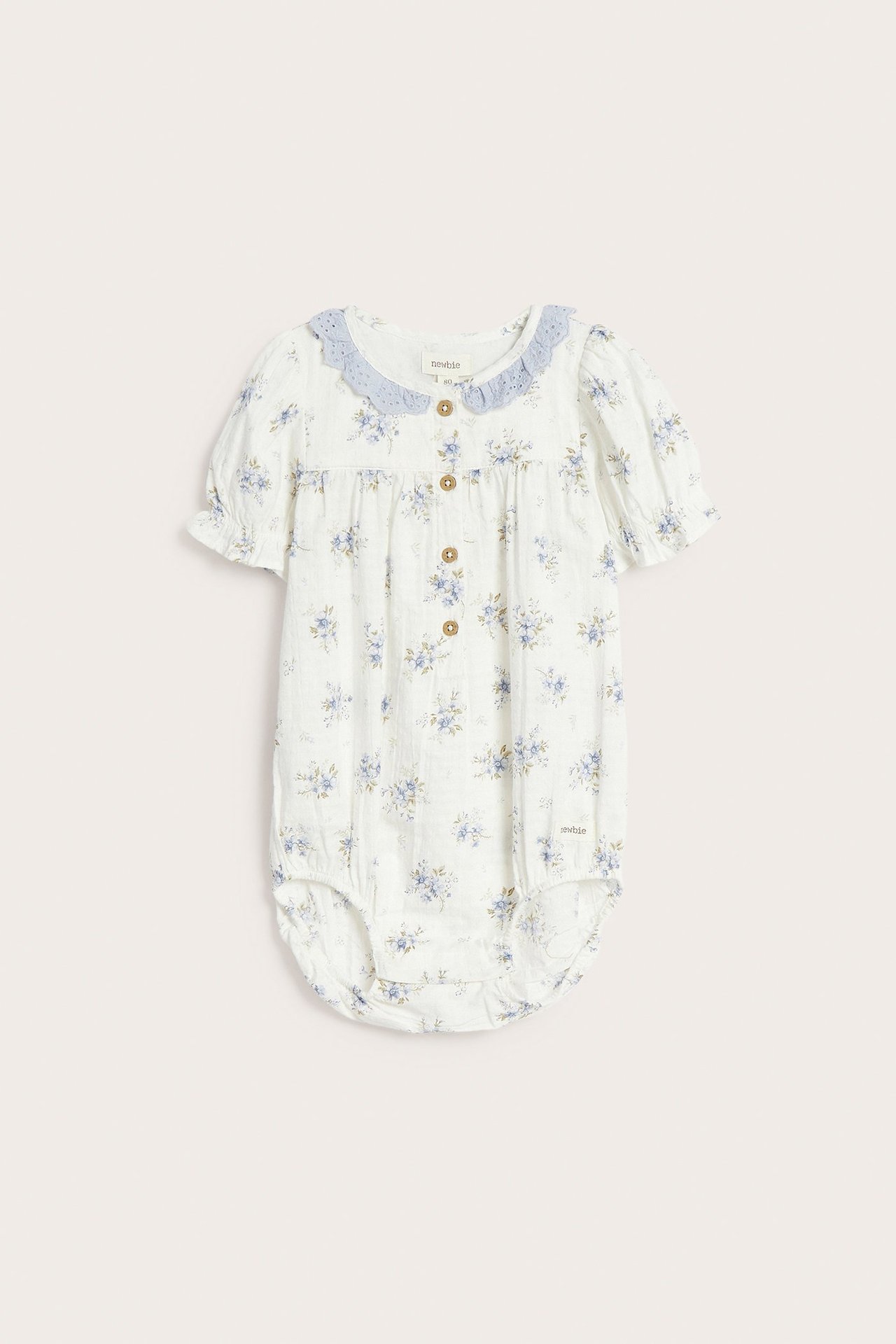 Vorderansicht eines cremefarbenen Baby-Bodys mit blauem Blumenmuster, hellblauem Spitzenkragen und kurzen Puffärmeln.