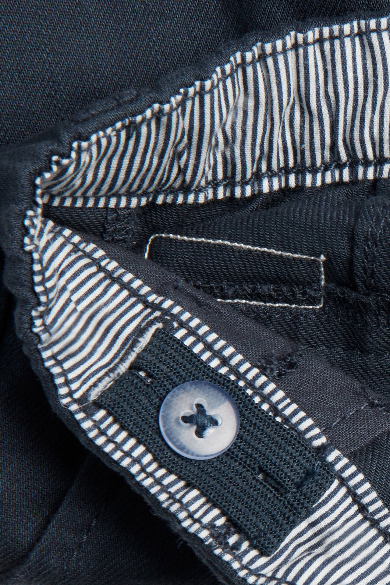 Close-up of dark blue cotton woven shorts with an adjustable elastic waistband and a striped inner lining.