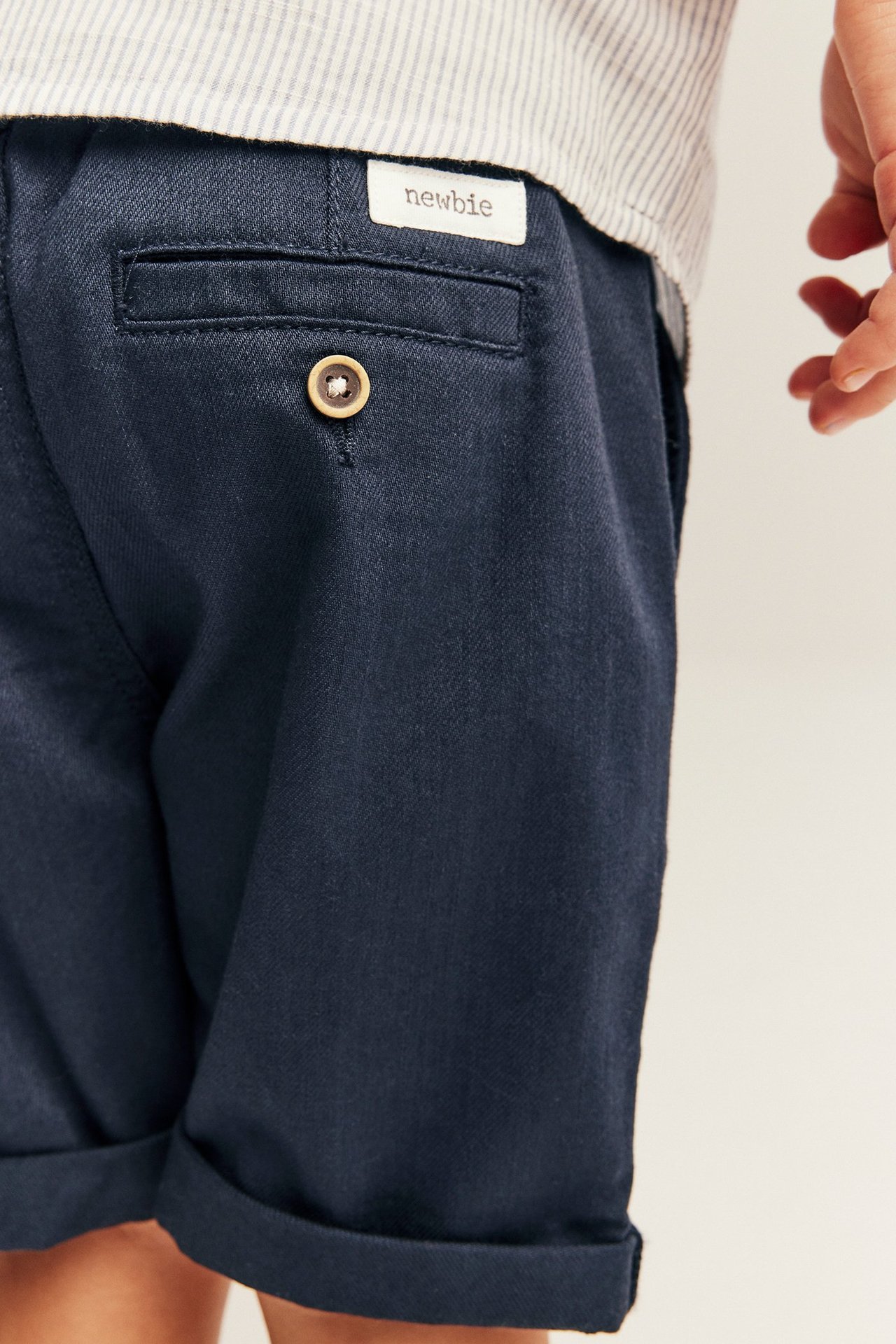 Close-up of kid wearing dark blue woven shorts with a buttoned back pocket and rolled-up legs.