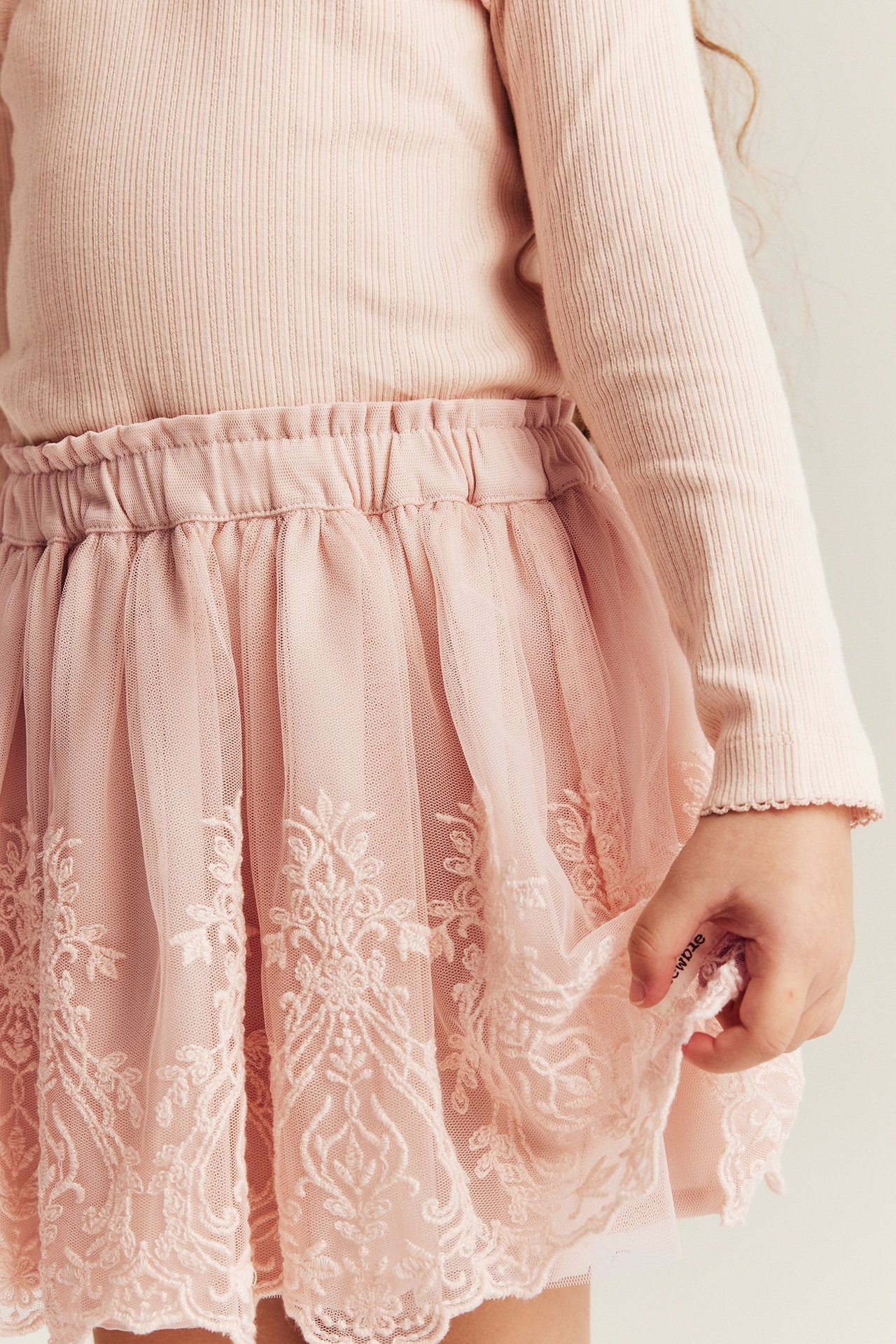 Close-up of a kid wearing a light pink embroidered mesh skirt and a light pink ribbed long-sleeved top.