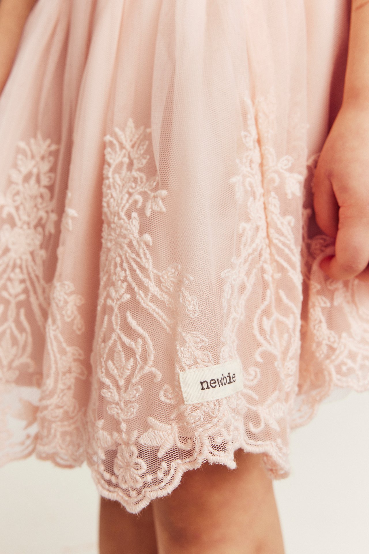 Close-up front view of a kid's light pink embroidered mesh skirt with a 'newbie' label.