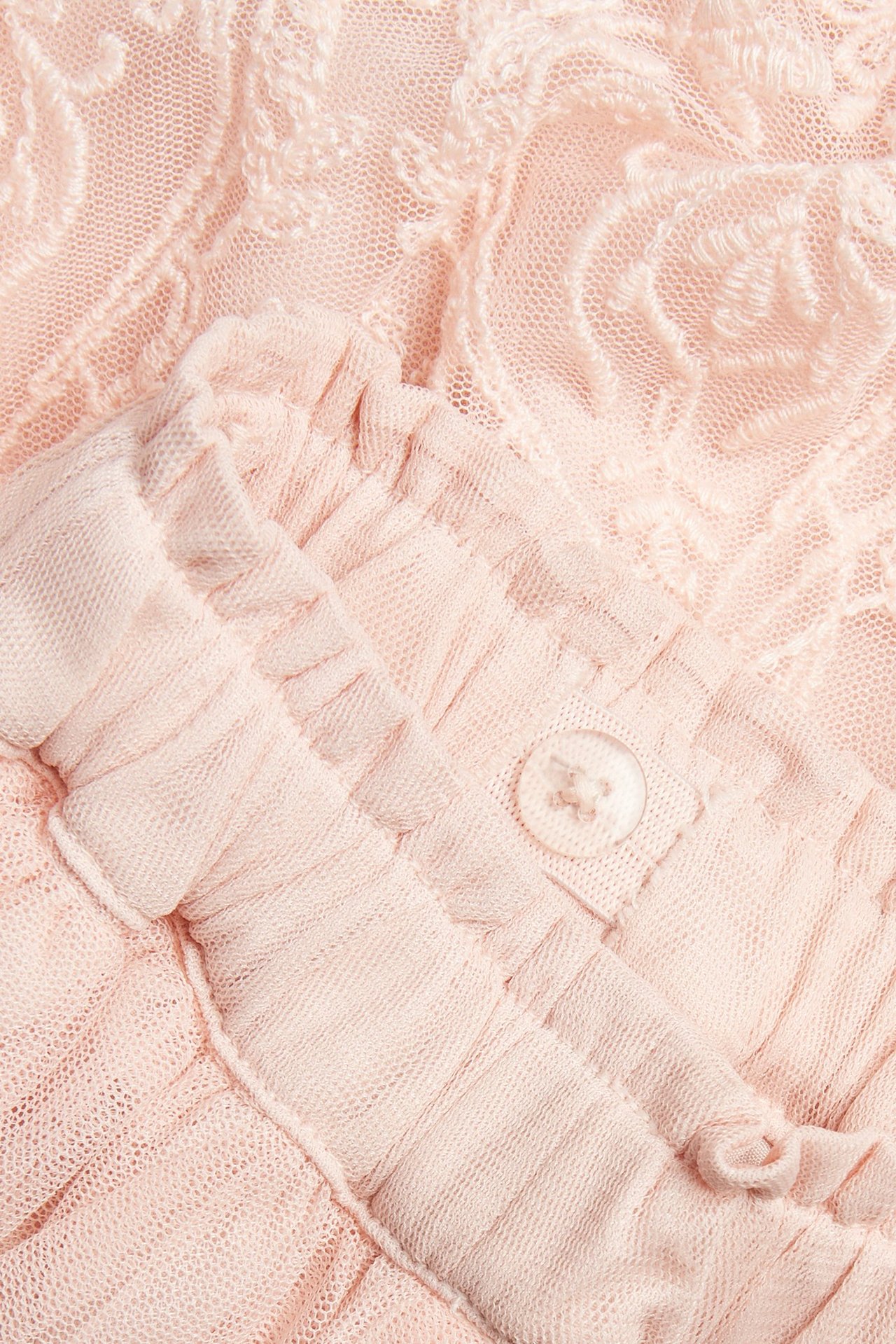 Nahaufnahme eines hellrosa bestickten Netzrocks mit Rüschendetails und einem Knopf.