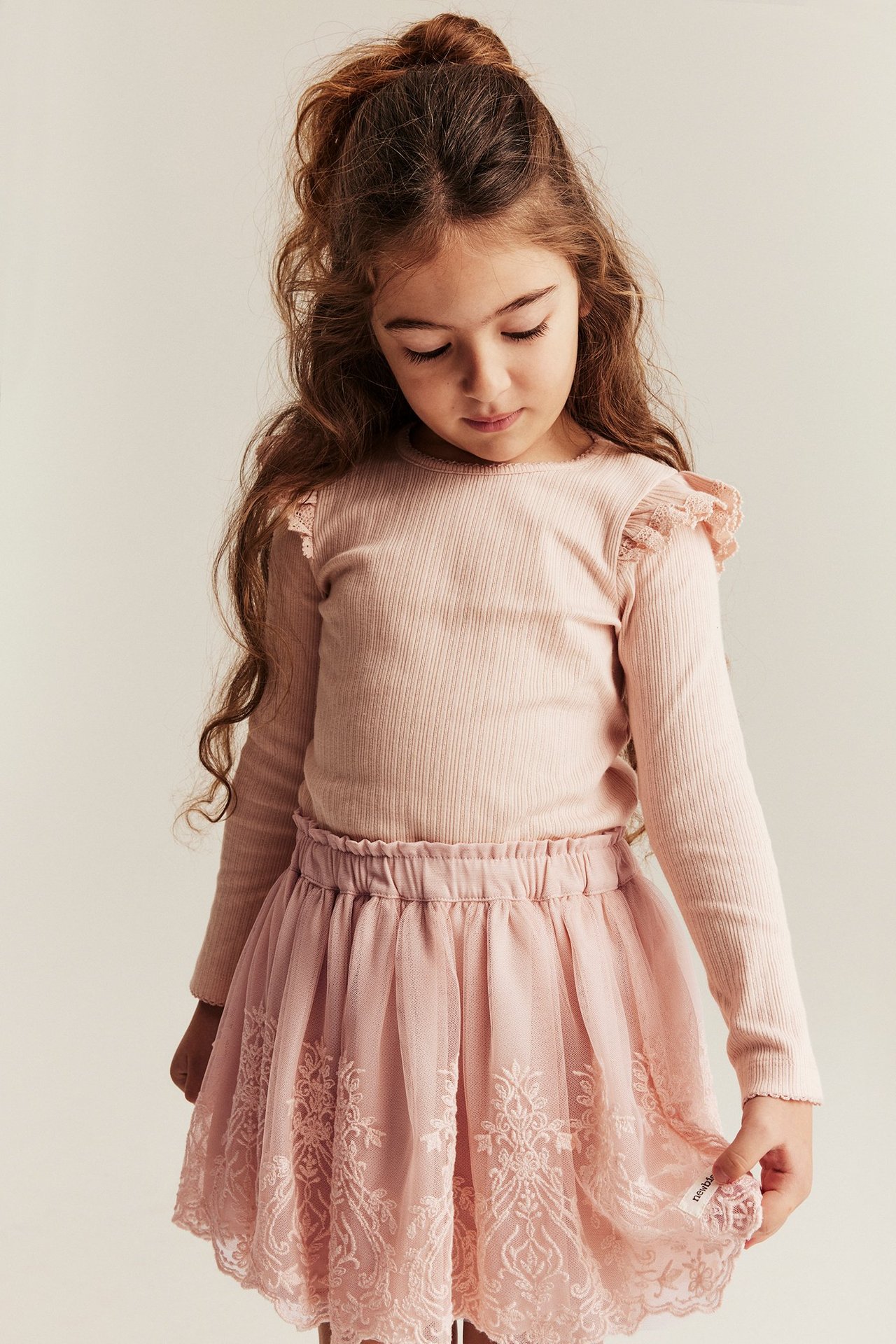 Front view of a kid in a light pink embroidered mesh skirt and a light pink ribbed long-sleeve top.