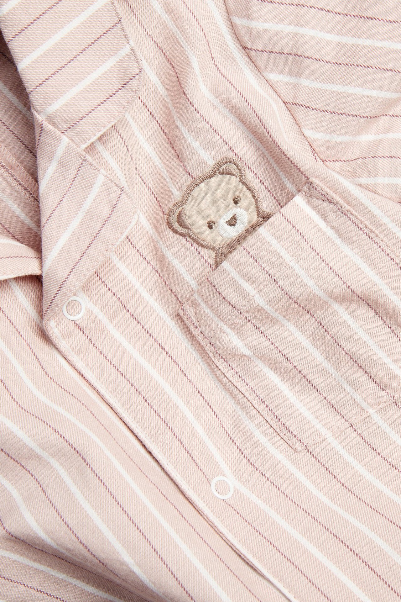 Close-up of pink and white striped cotton pajama top with teddy bear embroidery on chest pocket.