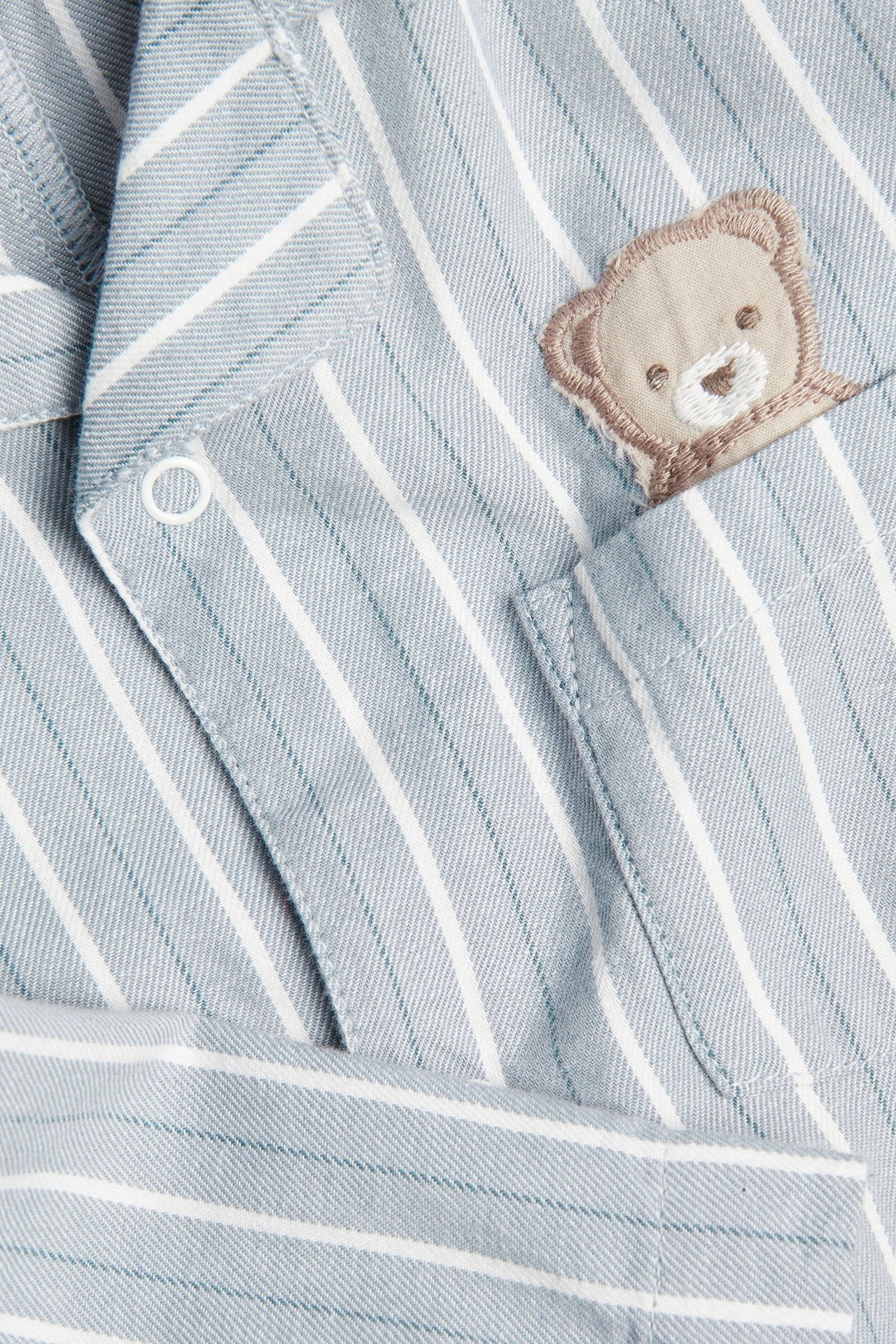 Nahaufnahme eines hellblau gestreiften Baumwollpyjamas mit Druckknopf und Teddybär-Stickerei.