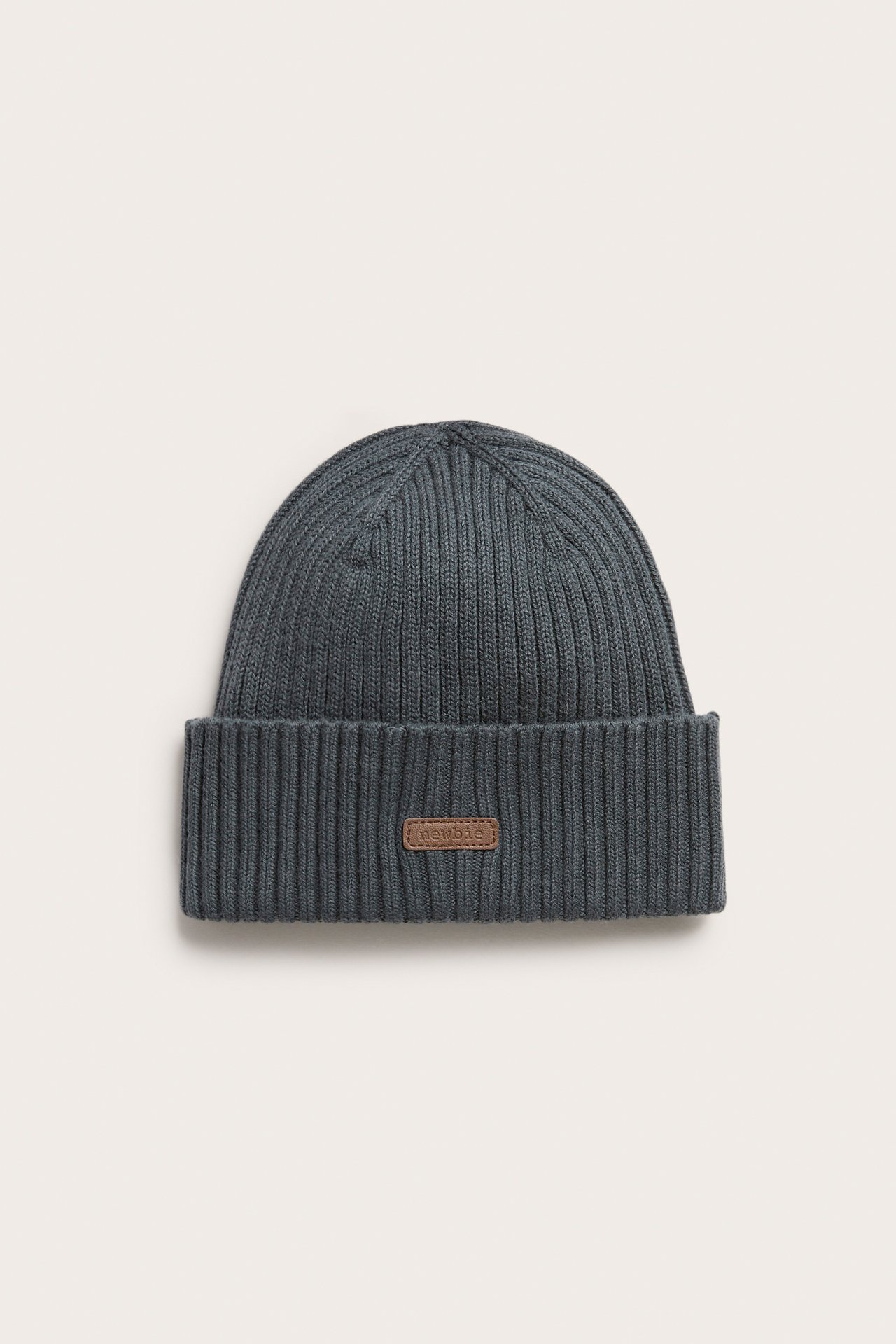 Front view of a dark blue rib-knitted cotton beanie with a fold-up brim and a small brown label.